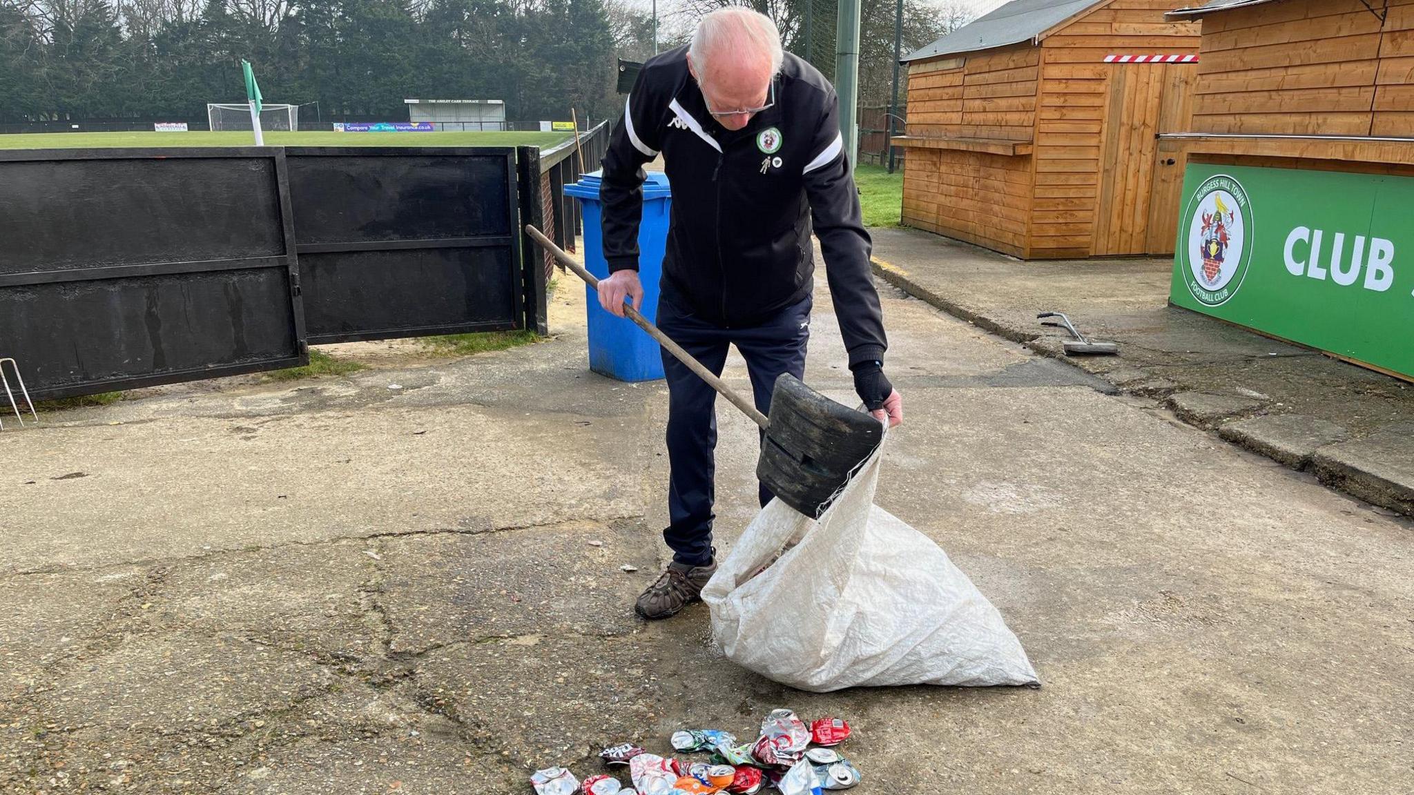 A man with short white hair bends down to pick up cans and put them in a bag.