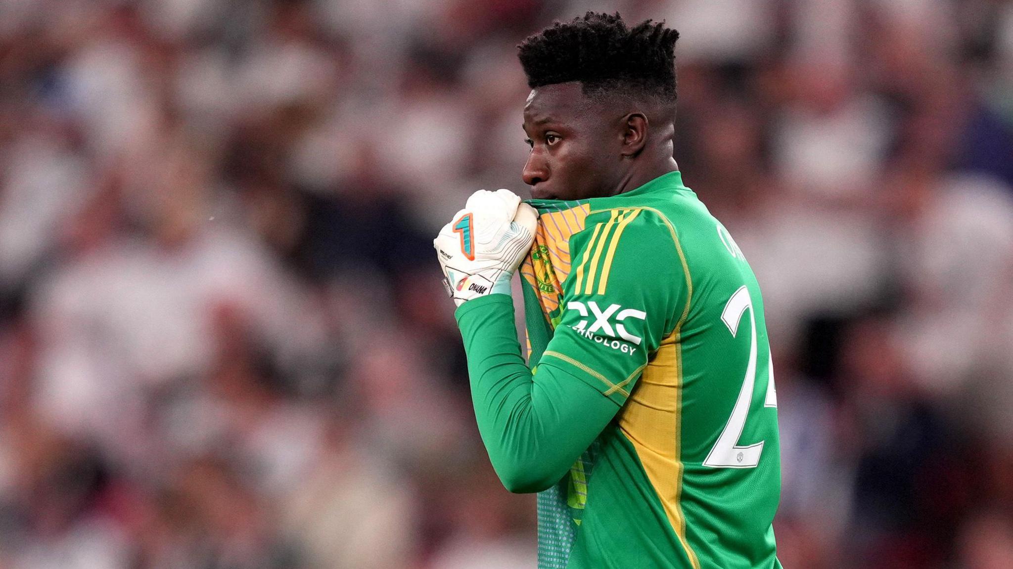 Andre Onana pulls up his green goalkeeping shirt to cover his mouth as he looks on during a football game