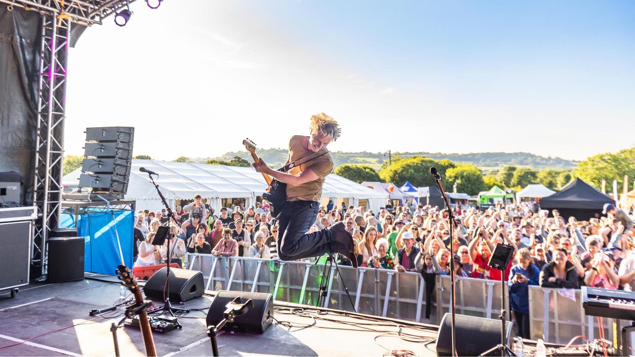 A crowd watching a man onstage with a guitar who is mid-jump