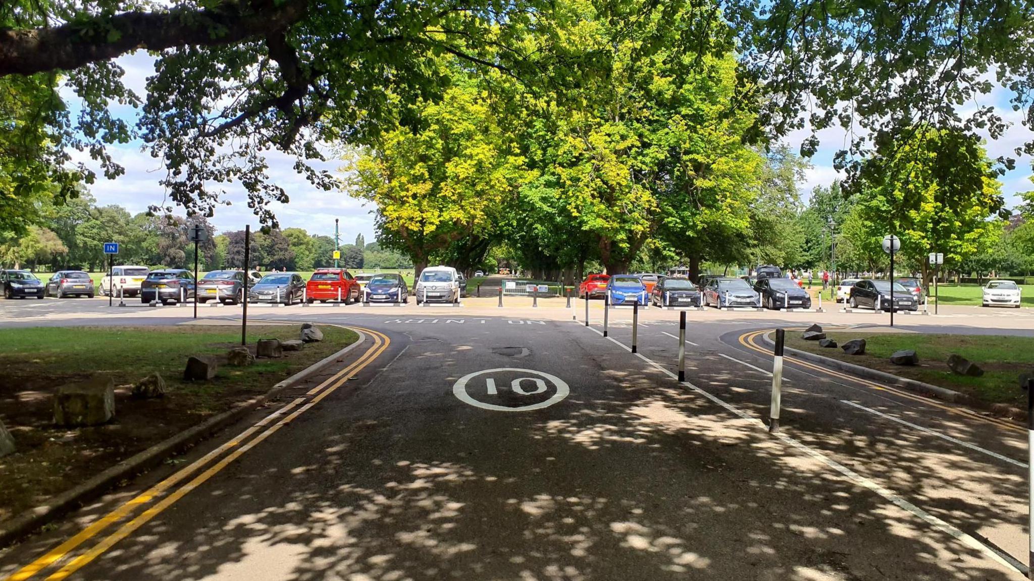 A road with road markings and bollards, with cars and trees in the distance.