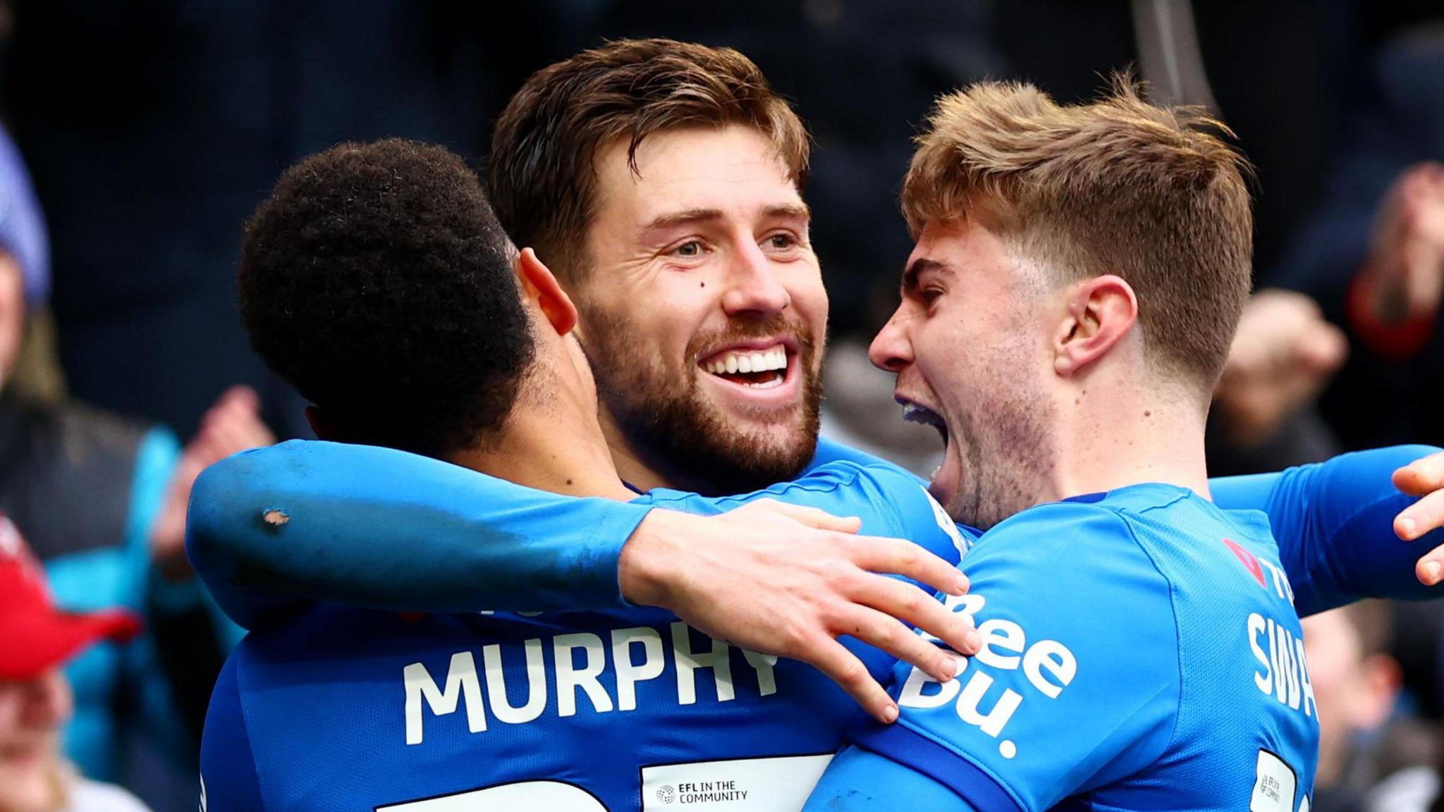 Callum Lang hugs two team-mates after scoring a goal