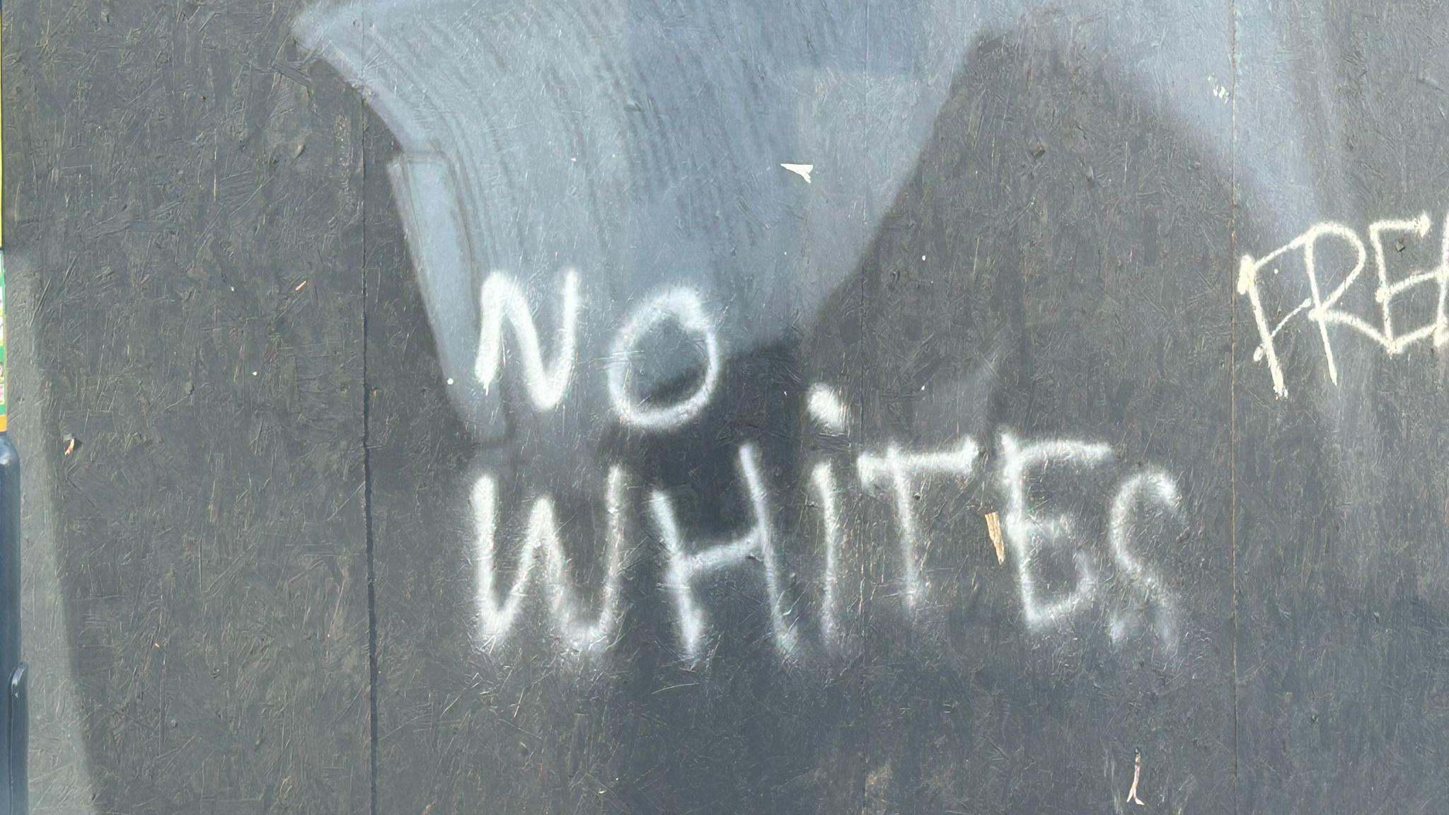 NO WHITES written in white paint on a hoarding on a wall