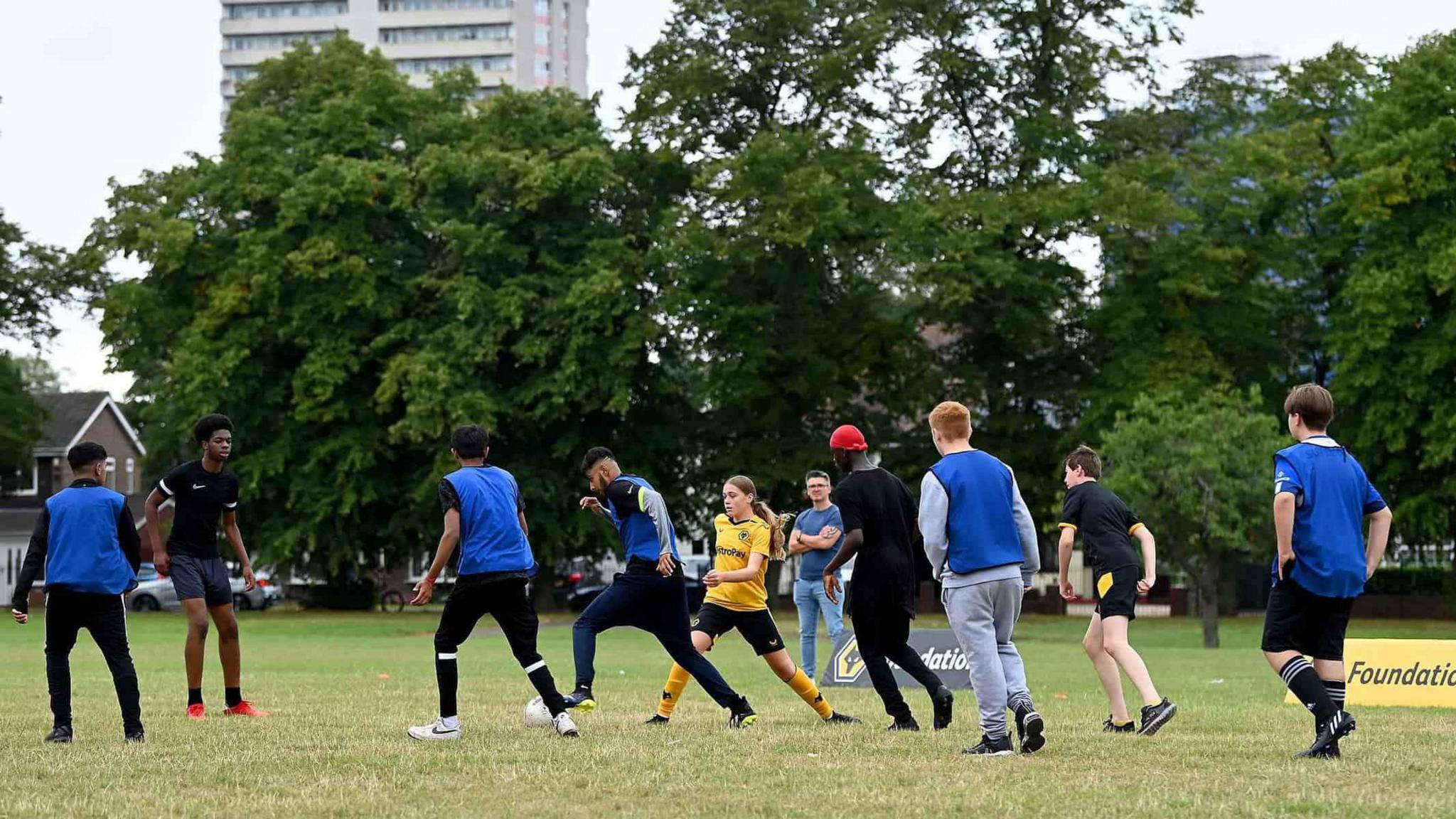 Children, some wearing blue bibs, play football in a park