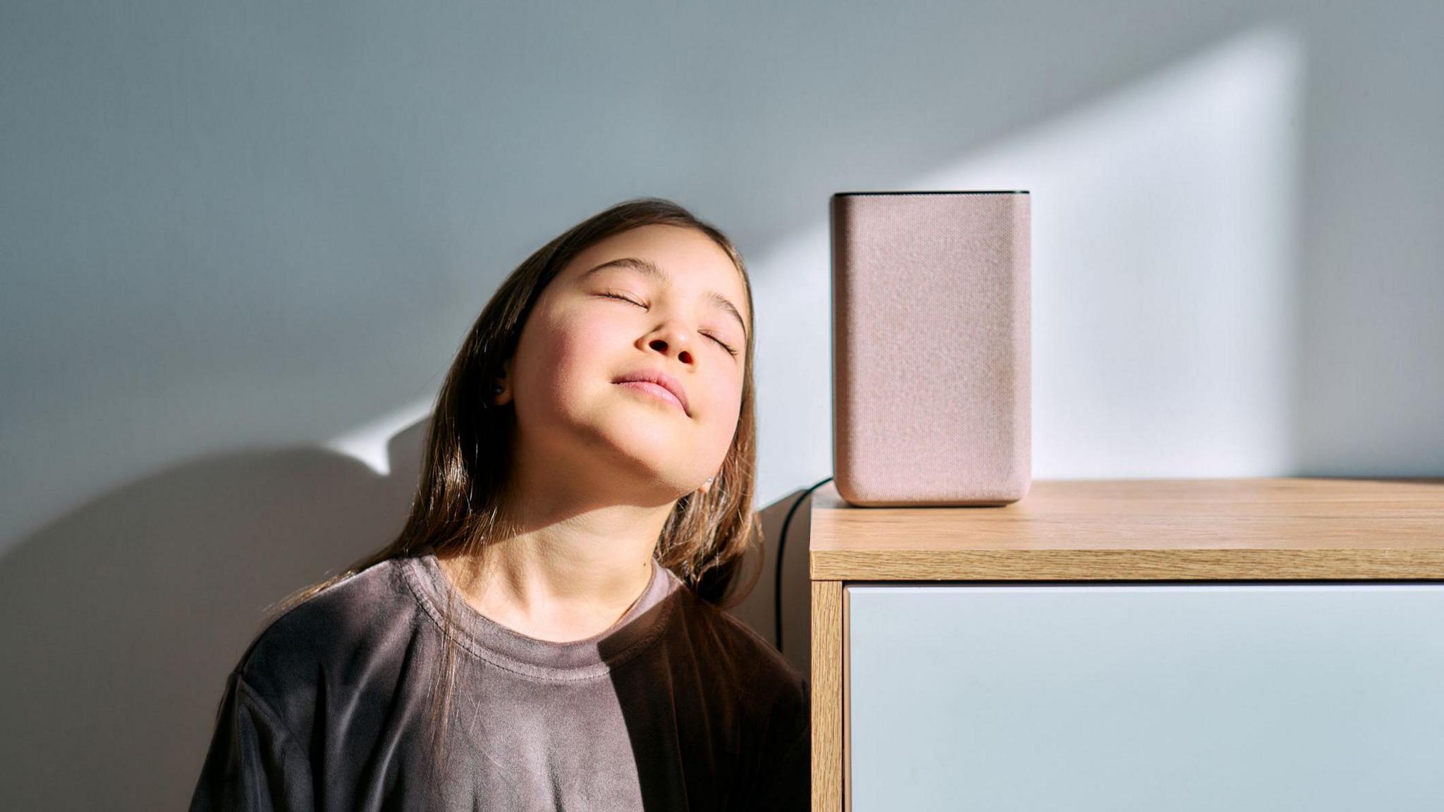 Girl stands by a speaker and closes her eyes as she listens. 