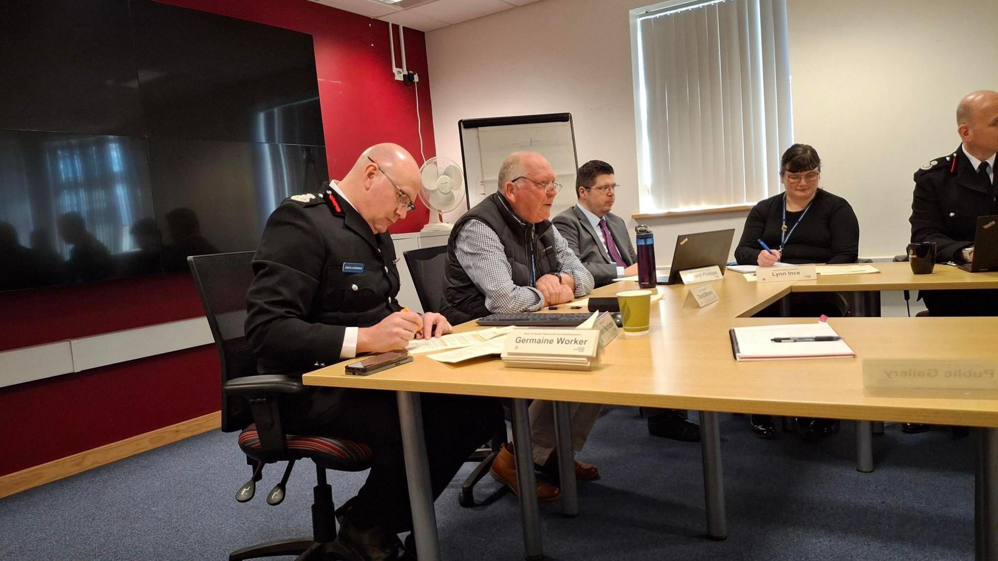 Men and women sit a desk during a meeting of the Shropshire & Wrekin Fire Authority. A TV can be seen in the background.