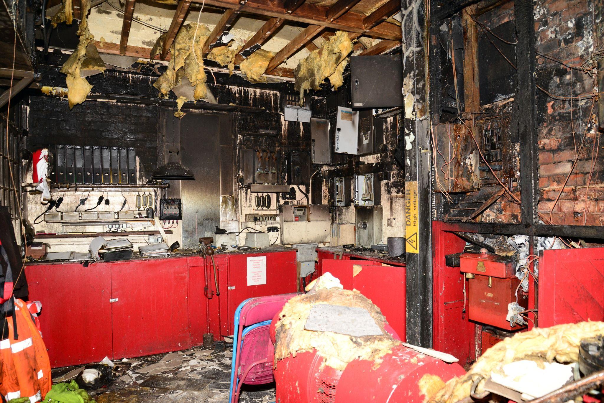 The fire damaged pump room has burnt out walls and insulation hanging out of the ceiling. The room had red cupboards and various electrical equipment on the wall, which all appear to be fire-damaged.