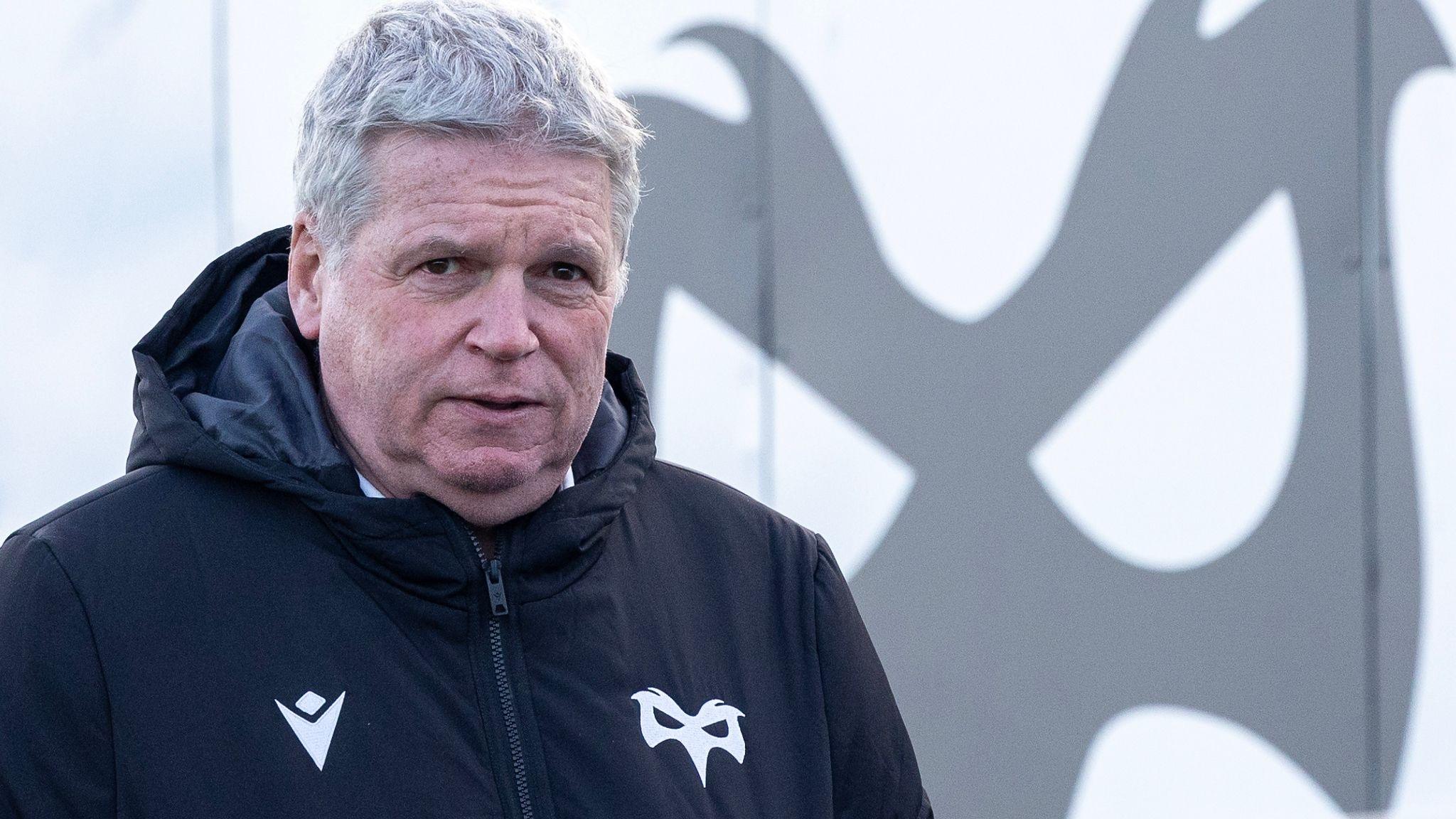 Lance Bradley in a black Ospreys coat in front of an Ospreys logo