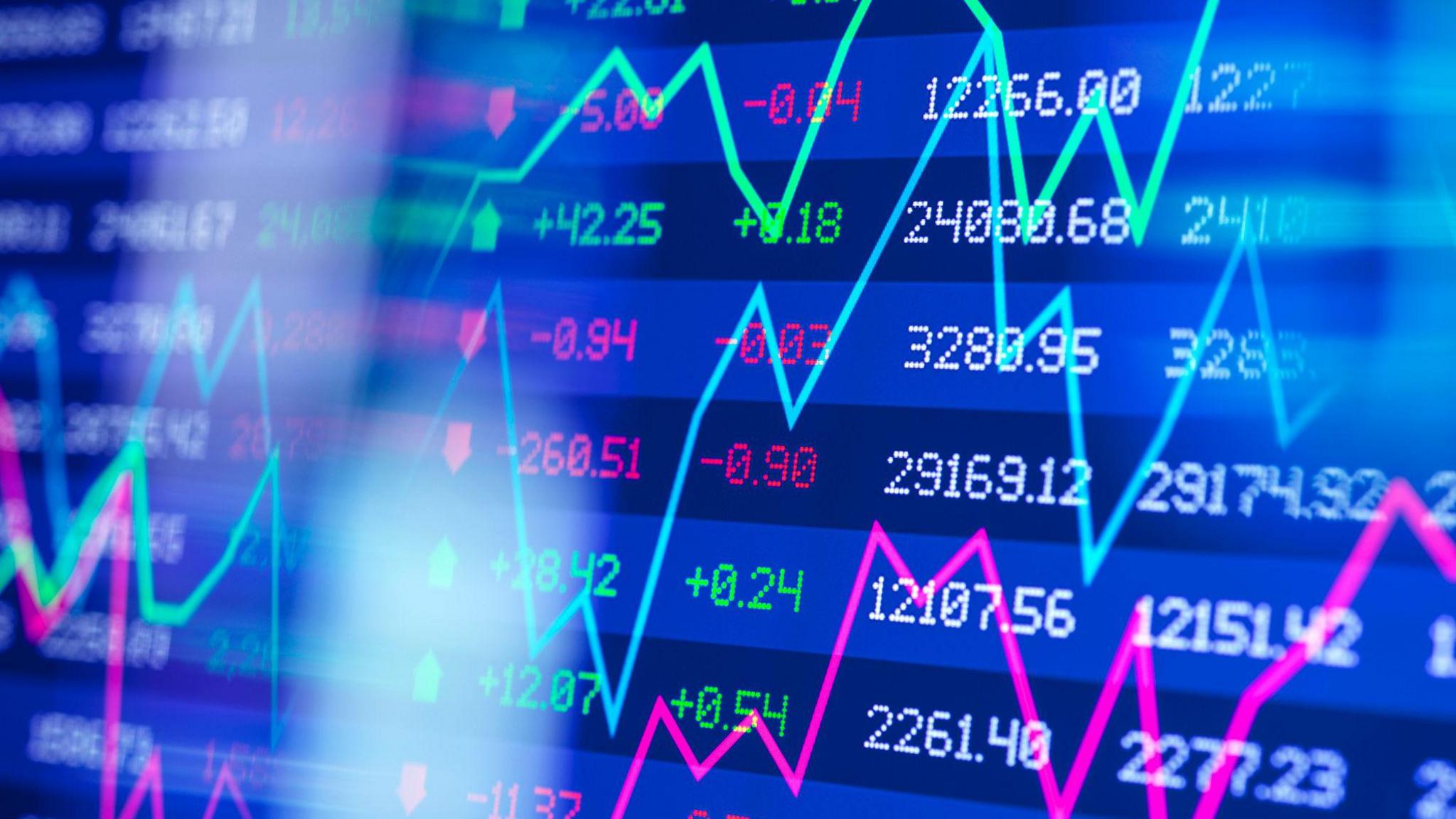 Performance of stock shares on screen. There are columns of numbers in red, green and white. There are also graph lines across the screen. 