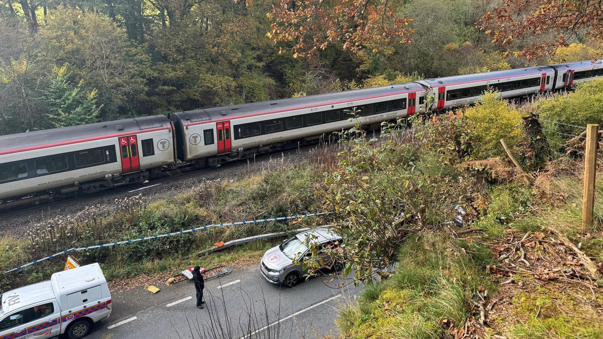 One RAIB vehicle and one TfW car pictured on the road adjacent to the rail tracks alongside the train, with a standing investigating officer. 