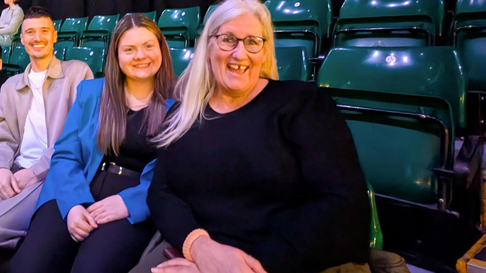 Two pupils sit next to choir leader Mandy Davison. They are sitting on plastic green arena seats at the MOBO Awards.