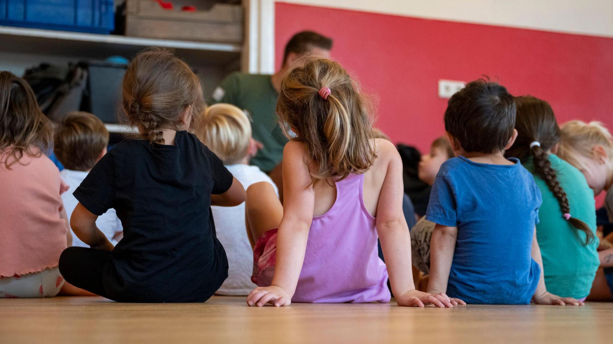 Children sitting on the floor attentively during story time, with their backs to the camera.