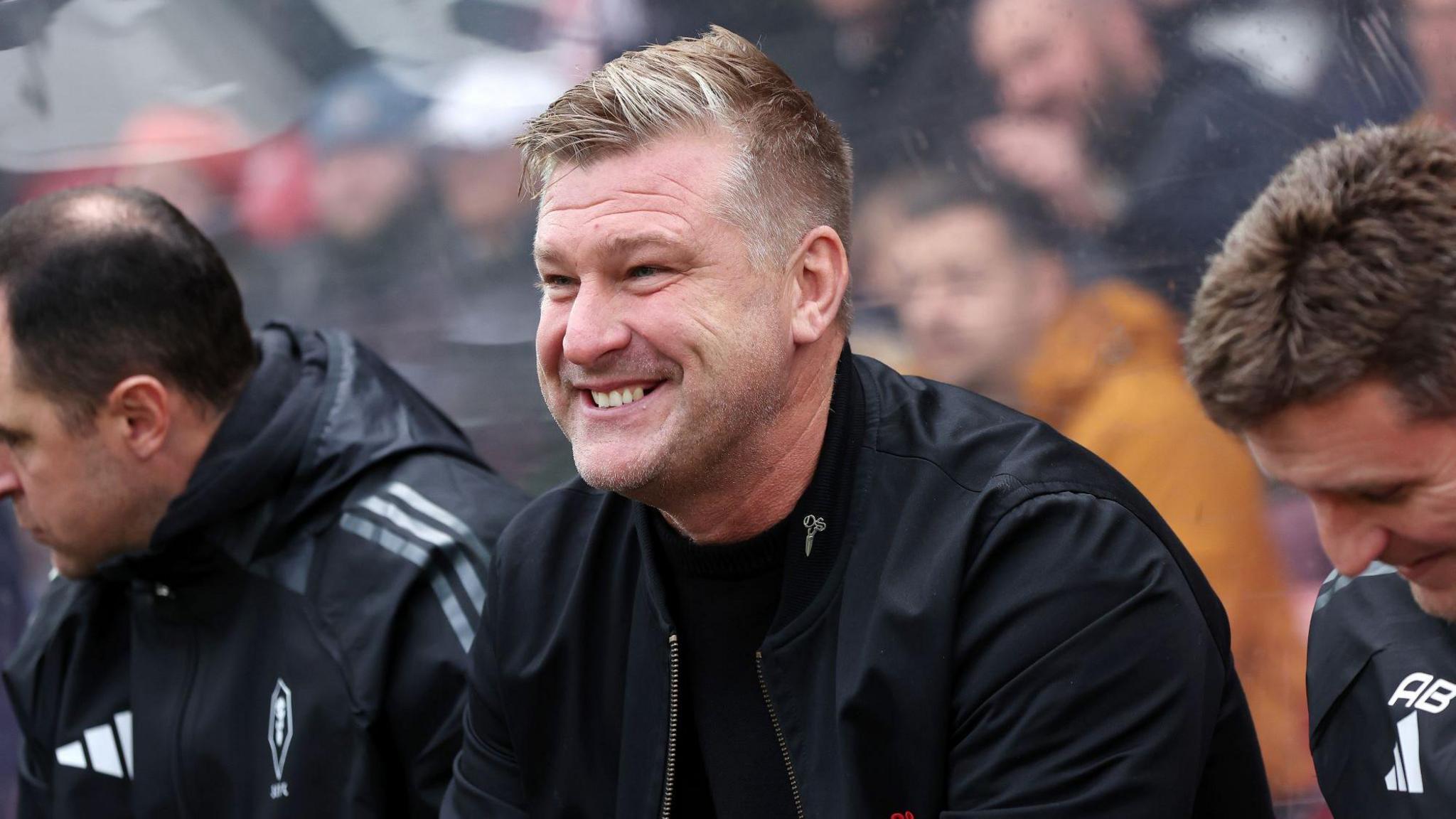 Karl Robinson sat in the dugout smiling during a match