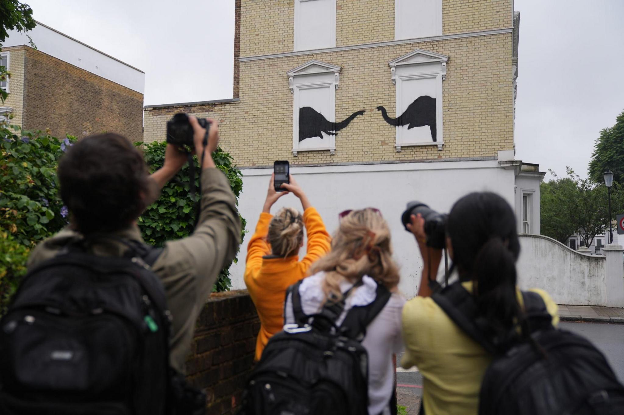 People photograph a new artwork depicting two elephants poking their heads out of blocked-out windows unveiled by Banksy 