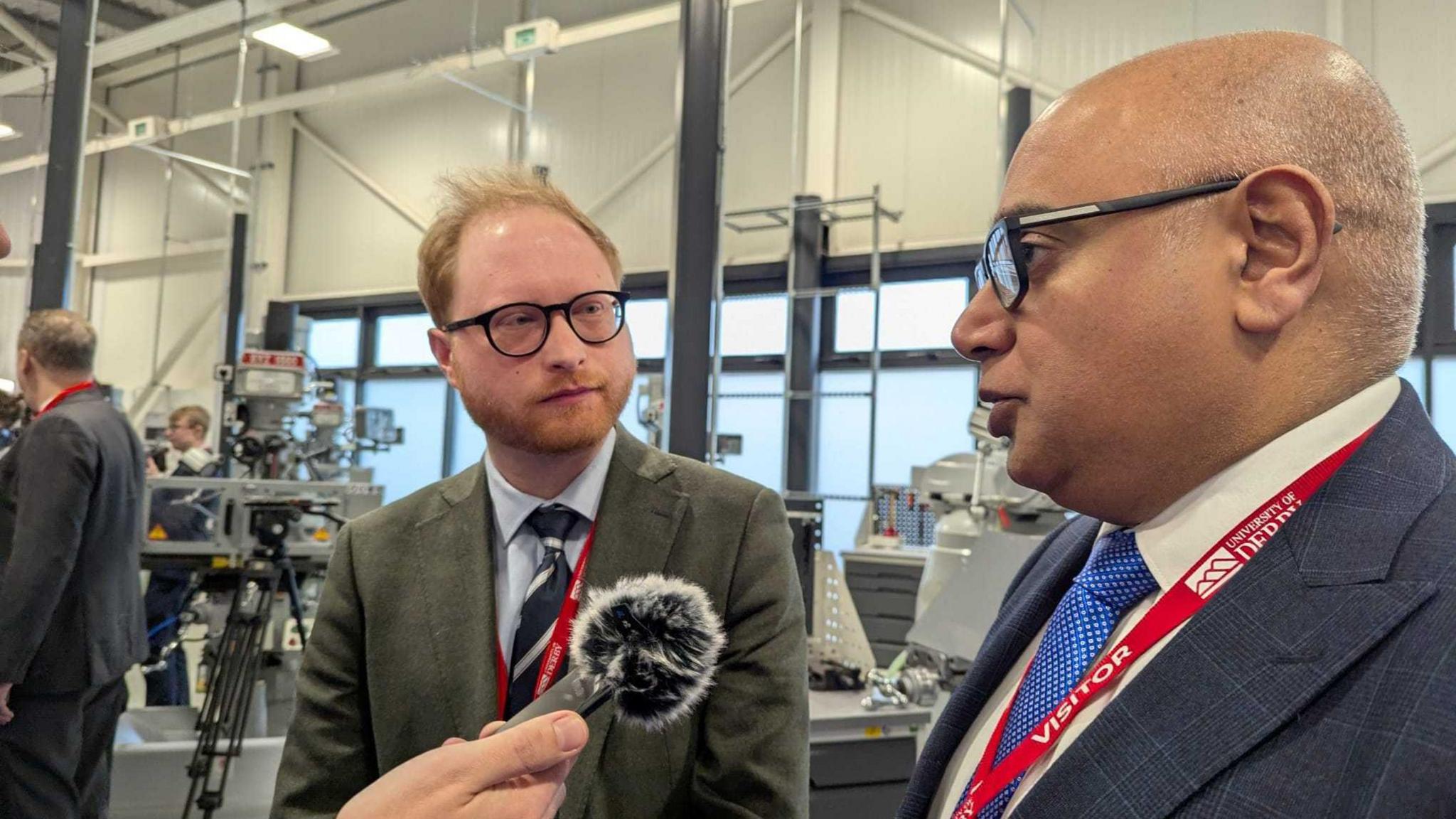 Mid-Derbyshire MP Jonathan Davies and Derby South MP Baggy Shanker stood talking. A microphone can be seen in front of  Baggy Shanker. They are both wearing suits and ties.