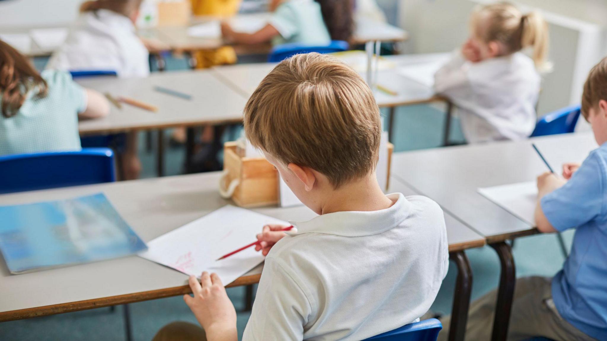 School boy sitting at a desk writing on a piece of paper