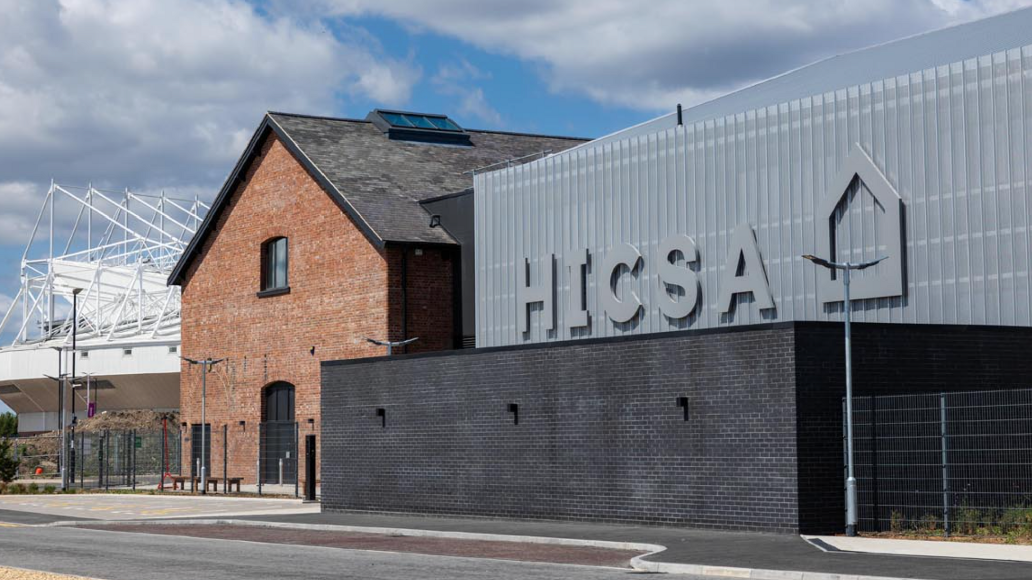 An external picture showing the HICSA and its proximity to the Stadium of Light. To the left of the photograph is the main building, which is the former goods shed, and to the right is the new addition which is grey in colour and has a sign which says HICSA.