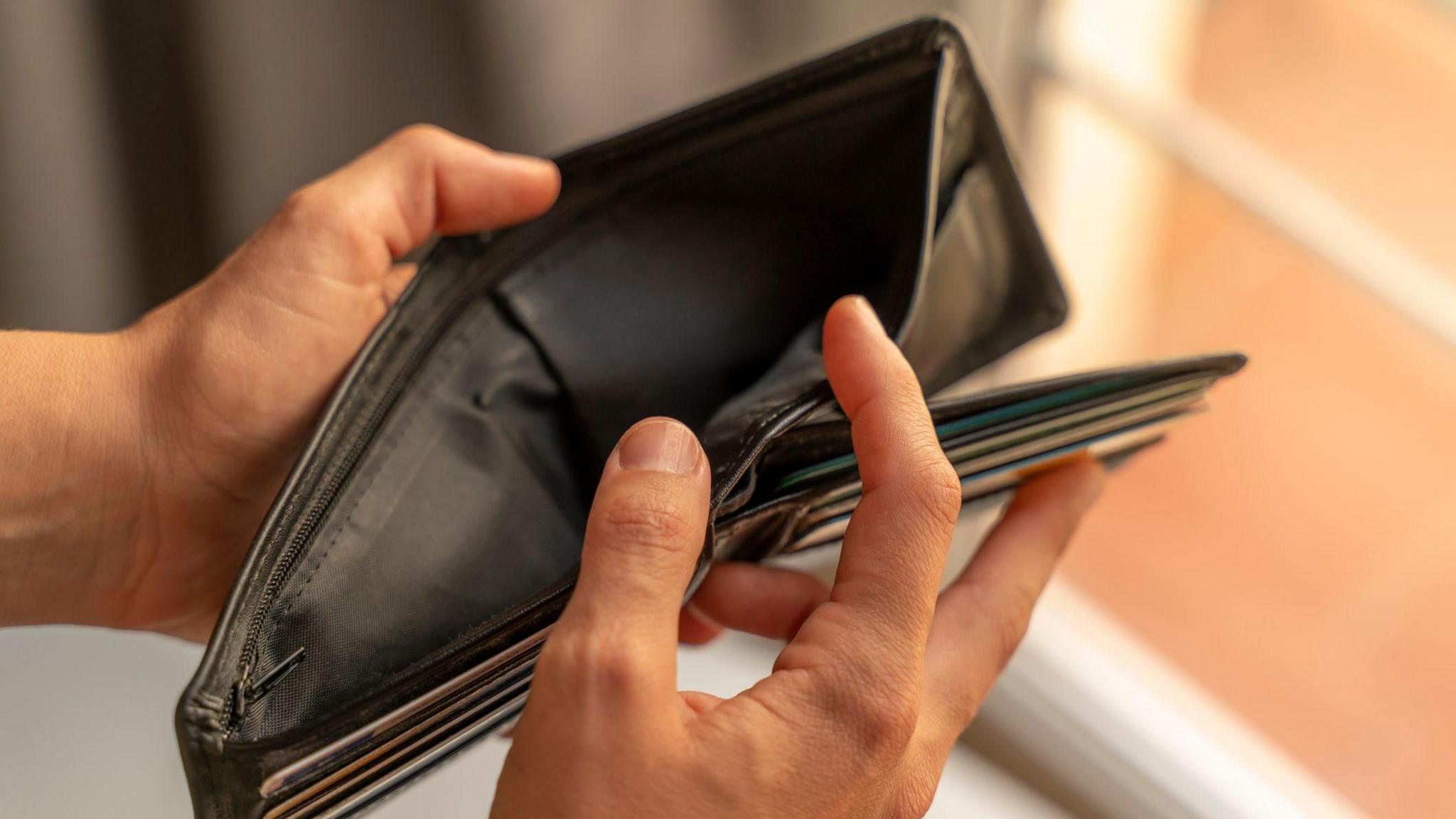 Brown wallet being opened, with two hands.