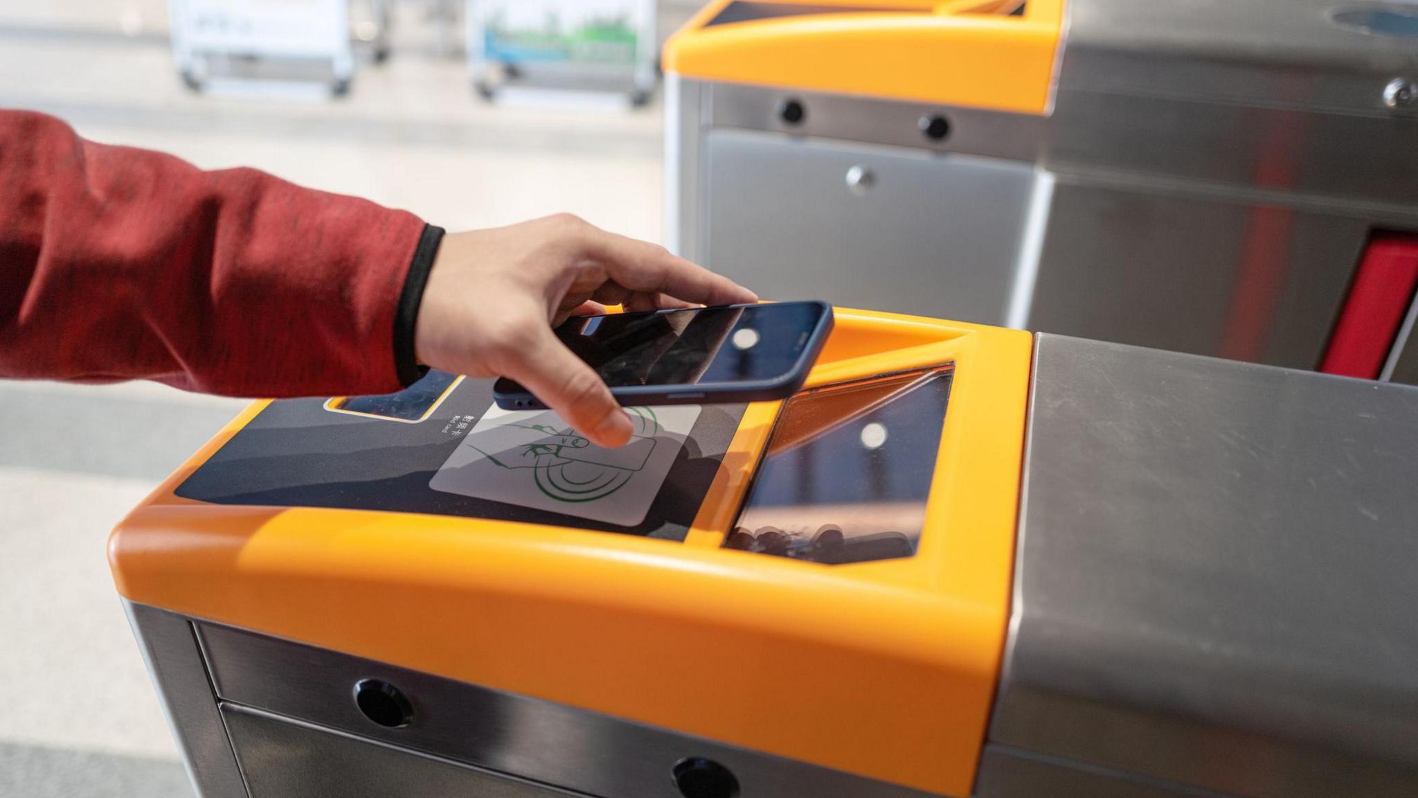 A phone screen is held above the screen of a ticket gate