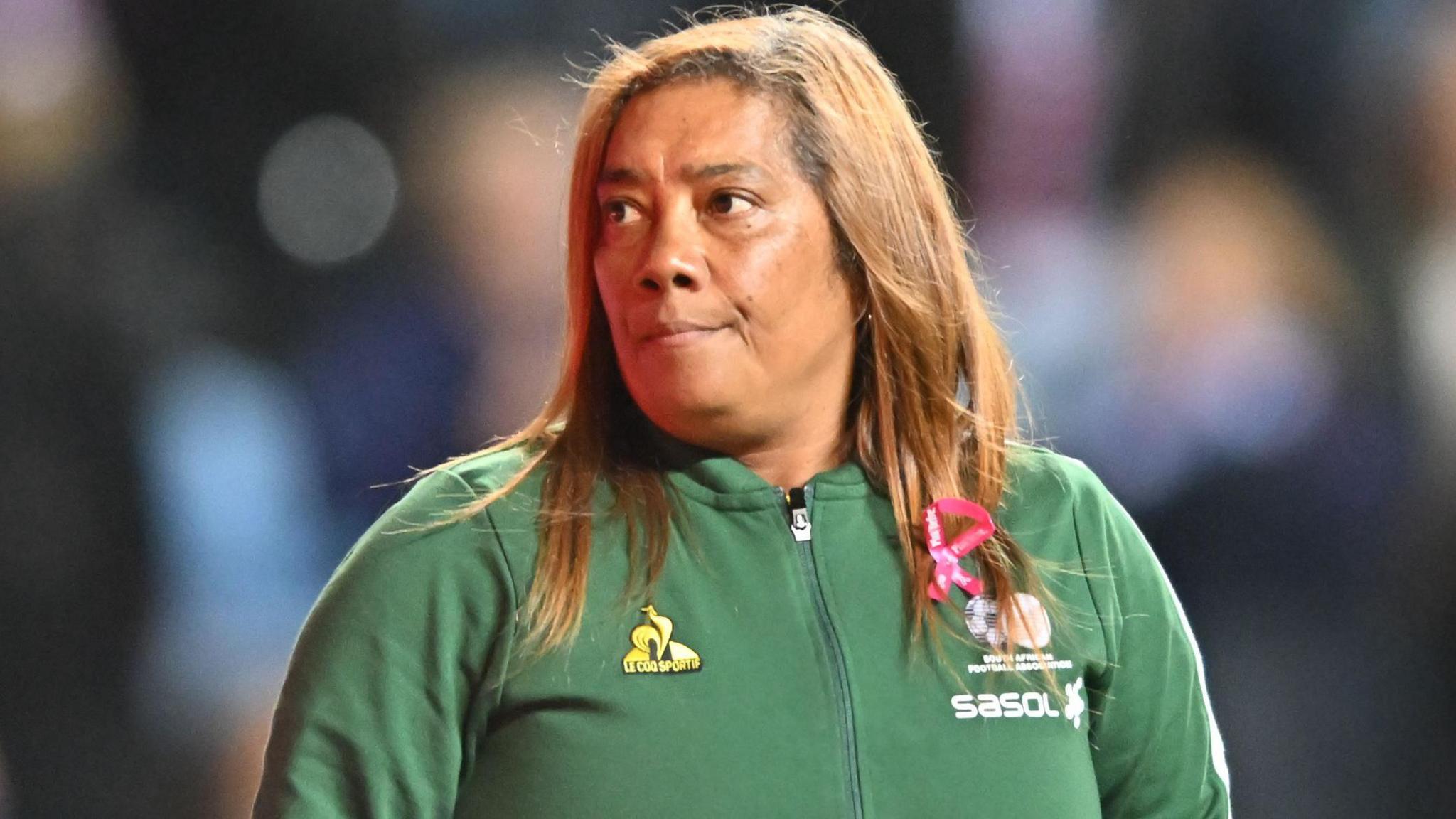 Desiree Ellis, wearing a green zip-up South Africa training top, looks to her right during a football match