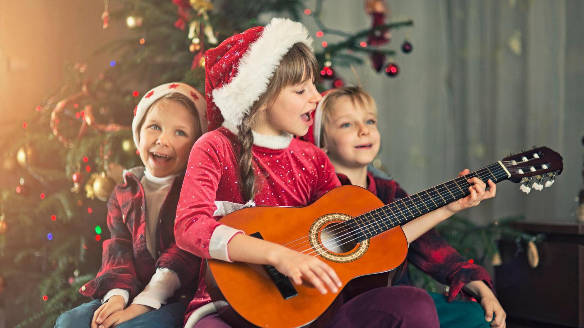 Little boys and little girl wearing santa's hat singing carols near christmas tree.