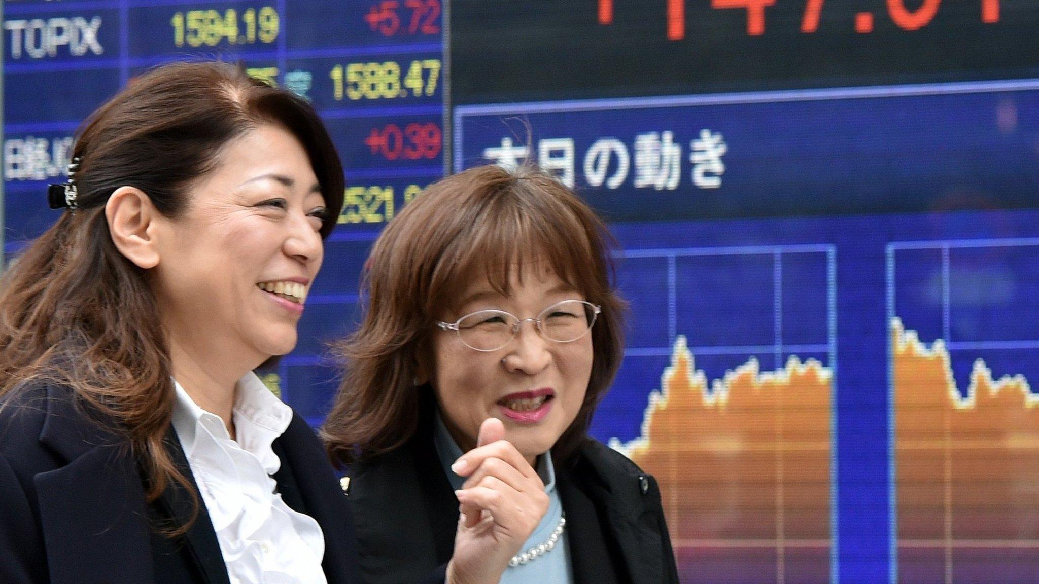 Pedestrians walk past a share prices board in Tokyo.