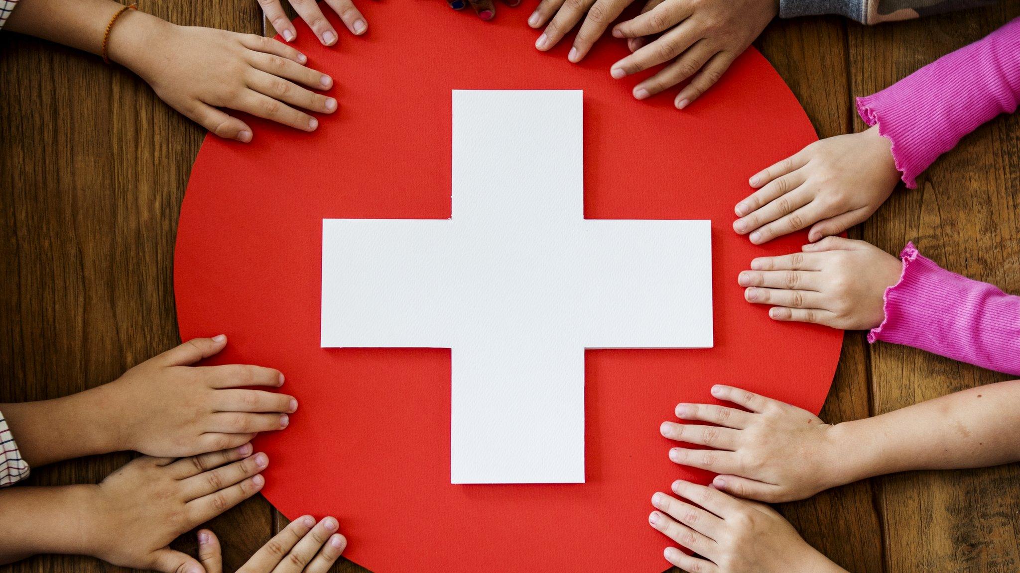 kids holding onto red cross sign