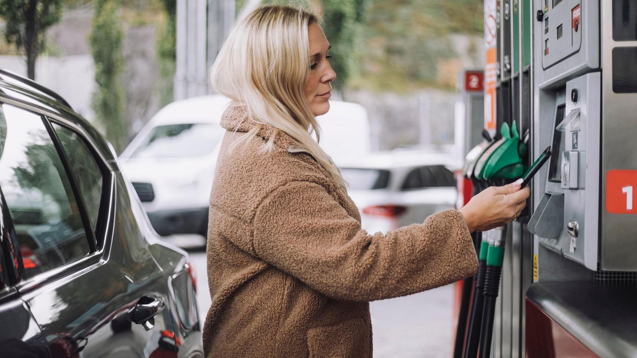 Blonde woman pays for petrol at pump with her smartphone