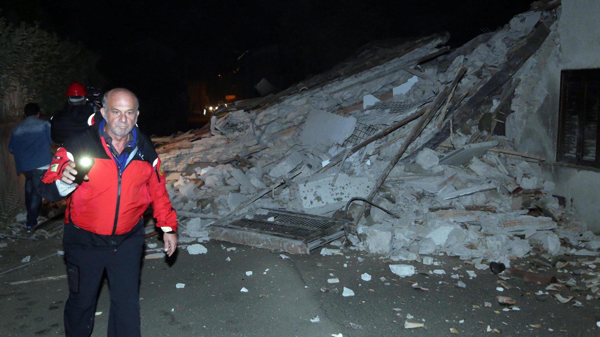 People walk past rubble as rescue operations begin in Villa Sant'Antonio village, near Visso, Marche region, Italy, on 26 October 2016