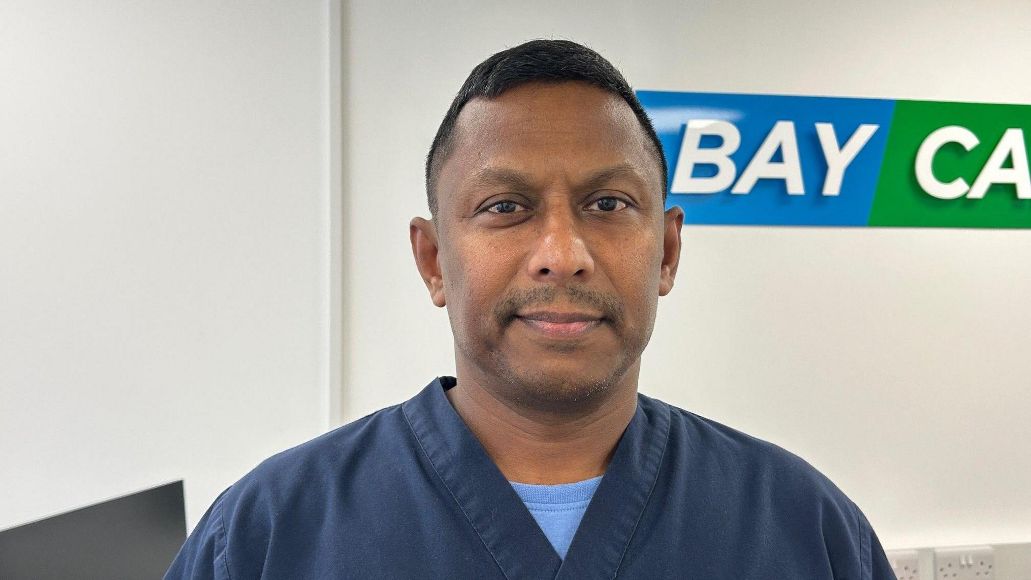 A man from Sri Lanka wearing a blue carers uniform