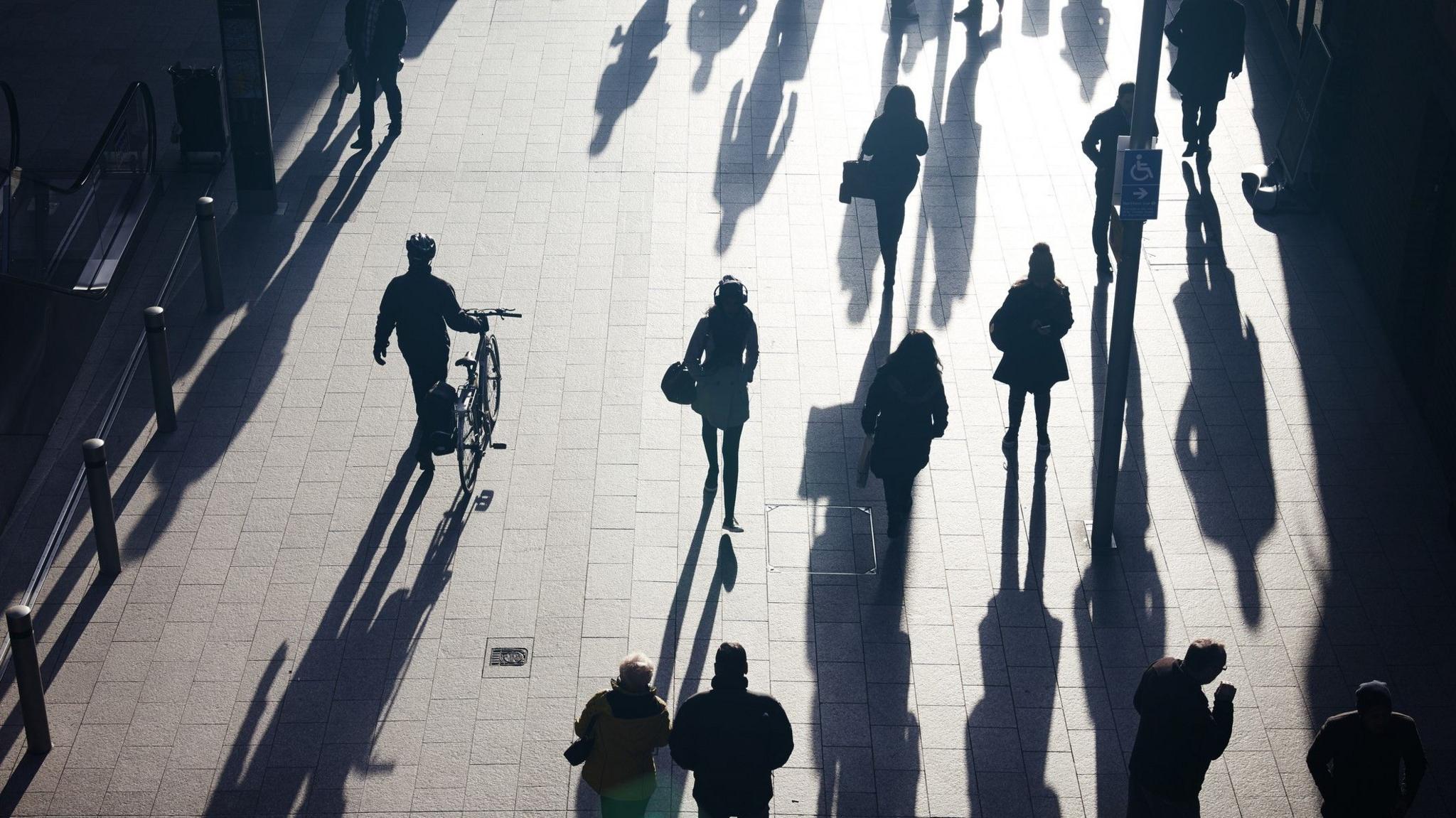 People's silhouettes seen as they walk over brightly lit pavement