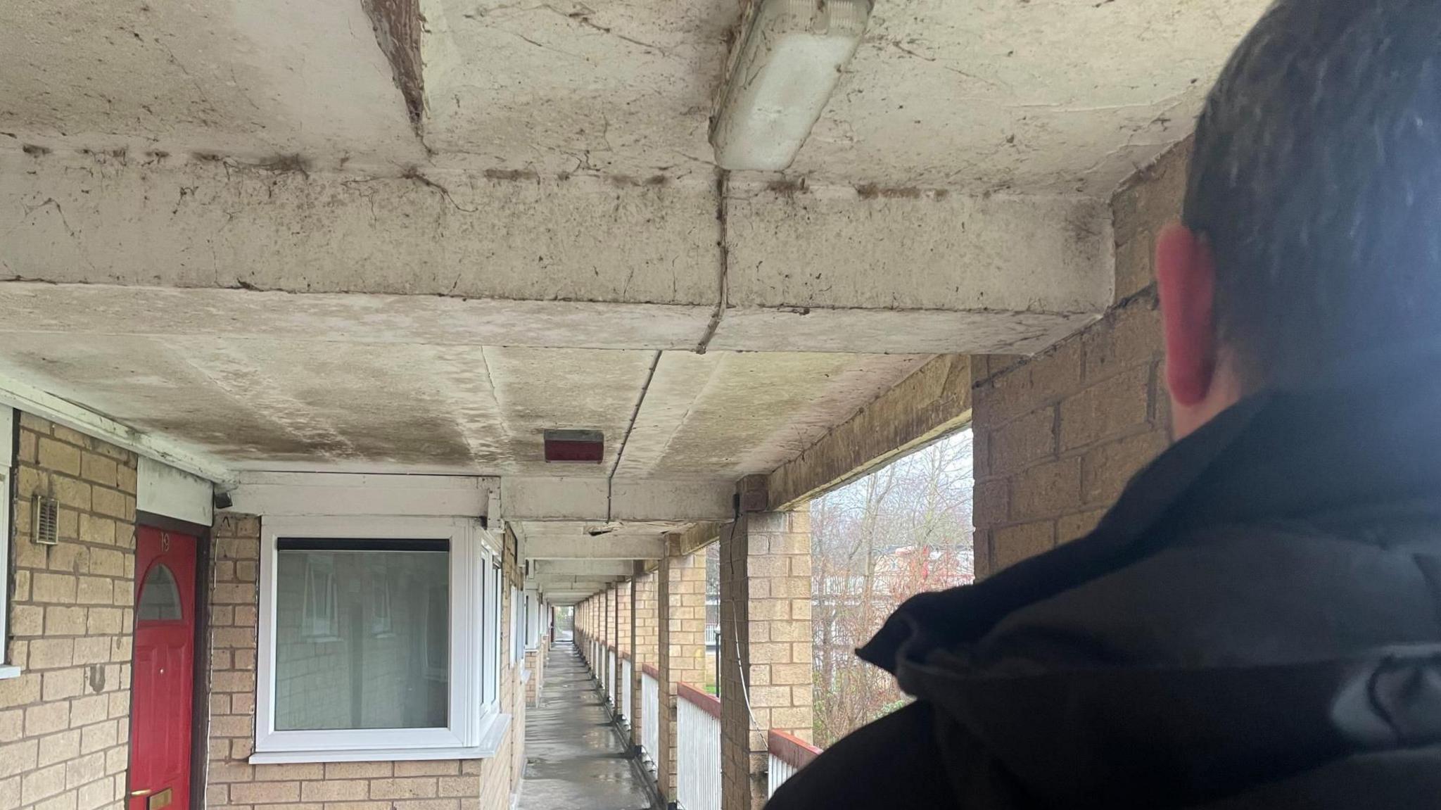 The back of a man's head as he looks down a corridor in a block of flats