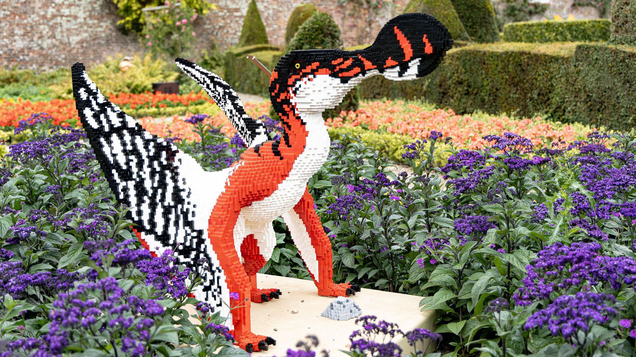 Another Lego dinosaur with large wings and beak sits within a flower bed at the stately home.