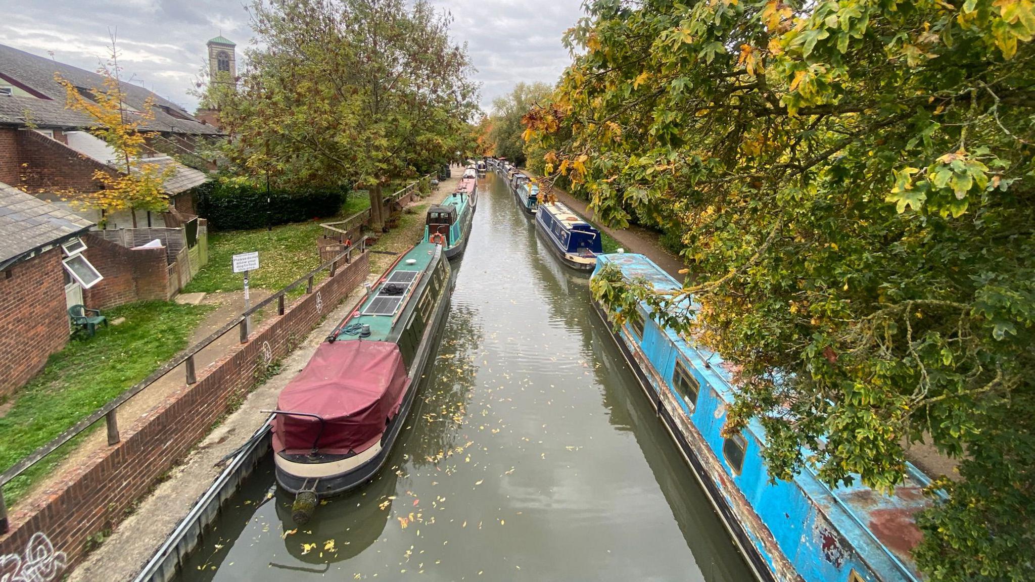 A view of the Mount Place bridge of the Oxford Canal during the Jericho Oktoberfest on 17 October. Several boats are lined up along the bank and trees. It is cloudy.