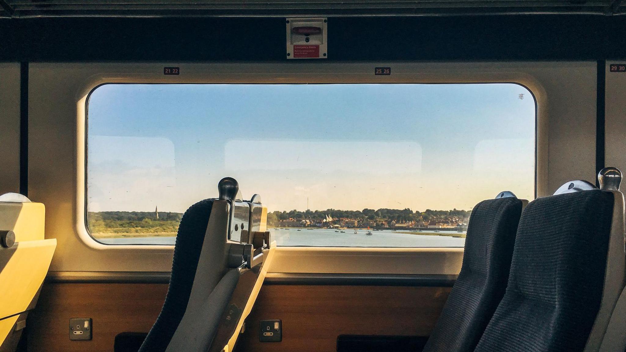 Side view of empty passenger seats in a modern train carriage interior with scenic coastal view out of the window at dusk.