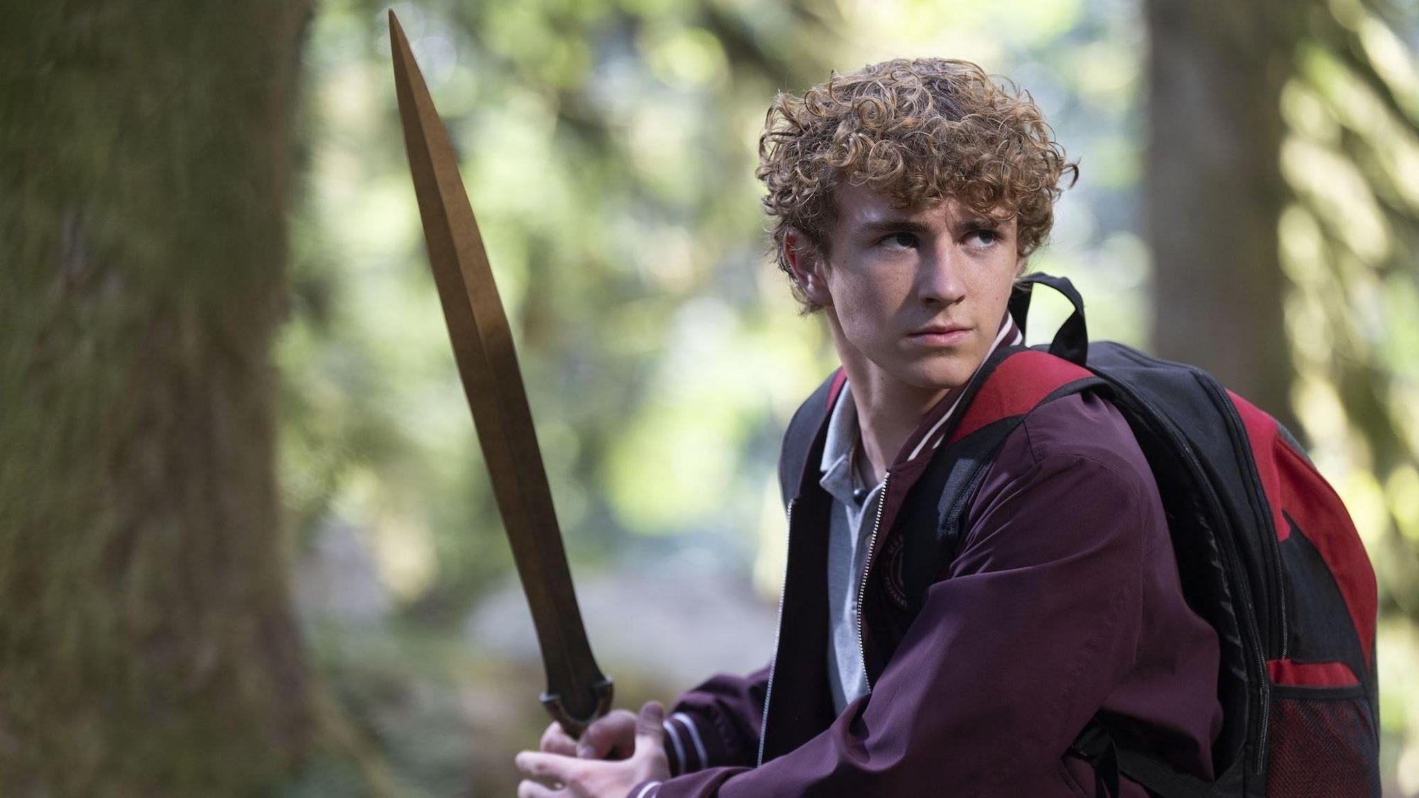 A schoolboy holds a sword in the woods.