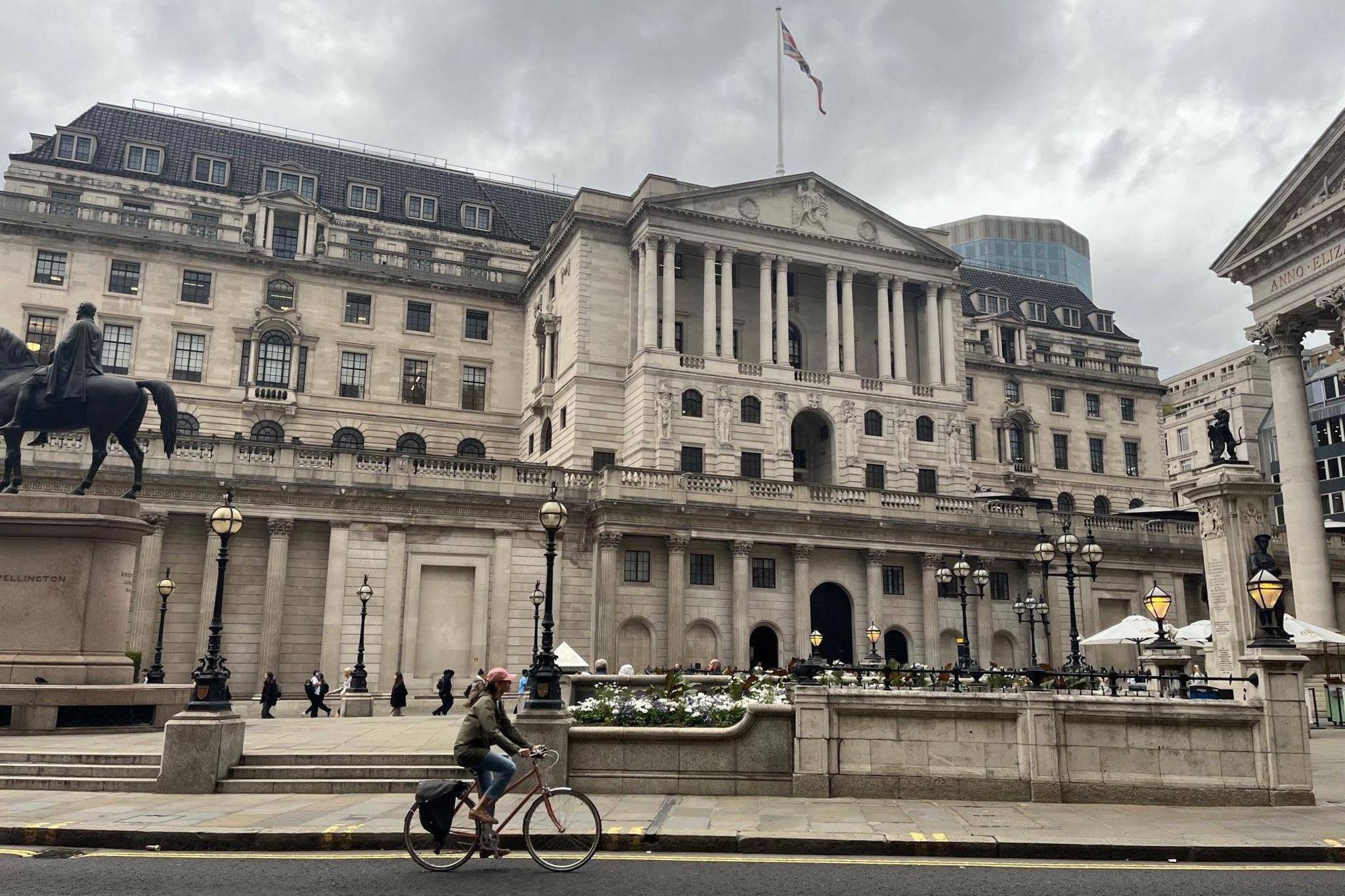A cyclist goes past the exterior of Bank of England which is covered with white Portland stone and has columns and sculptures all over the façade