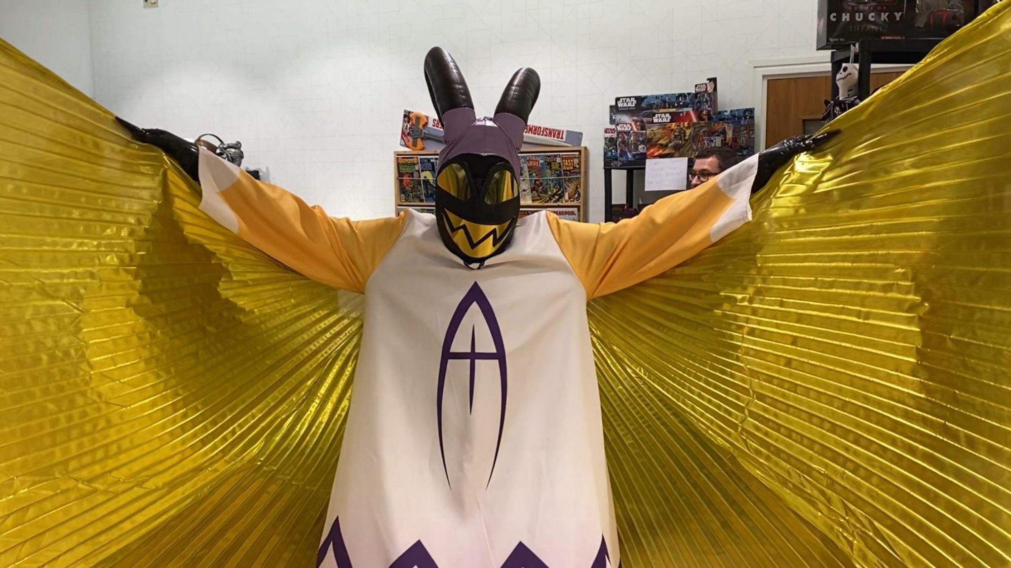 A person dressed up in a costume holds out their arms, displaying their golden wings. 