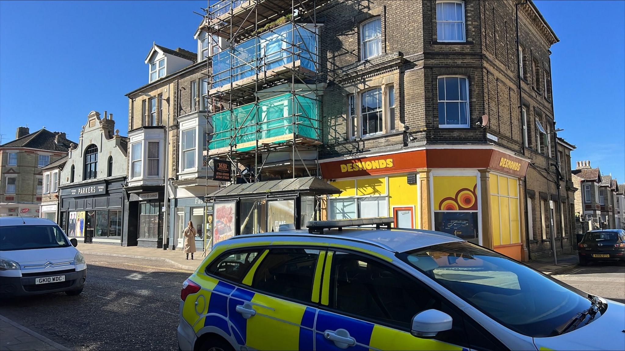 A police car is pictured outside a building which has scaffolding around part of it and a shop on the ground floor