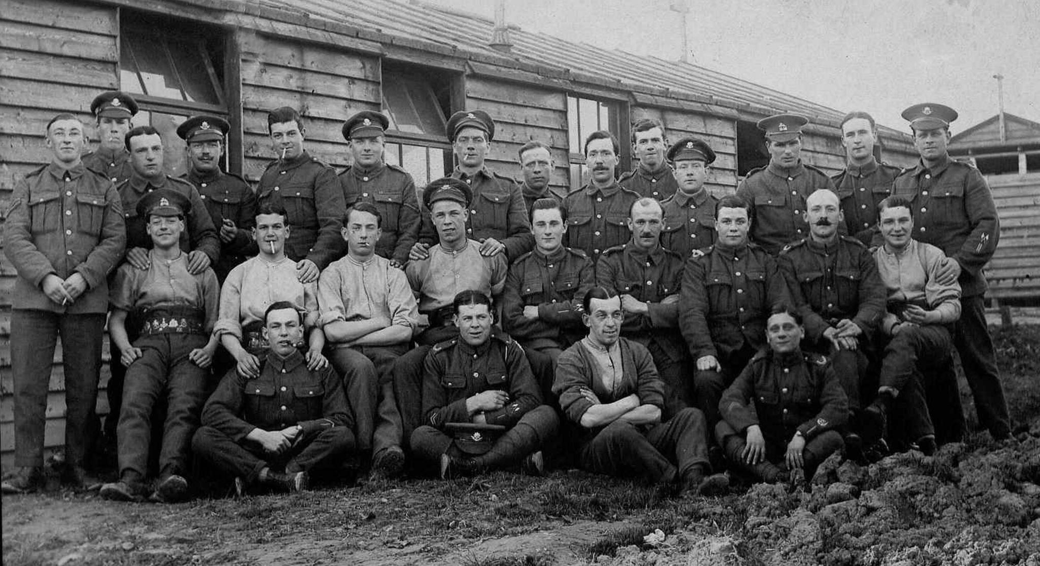 The black and white image shows soldiers in uniform posing for a group photo outside wooden buildings. It's believed to be A company of the 14th battalion of the Worcestershire Regiment and it was taken in 1916