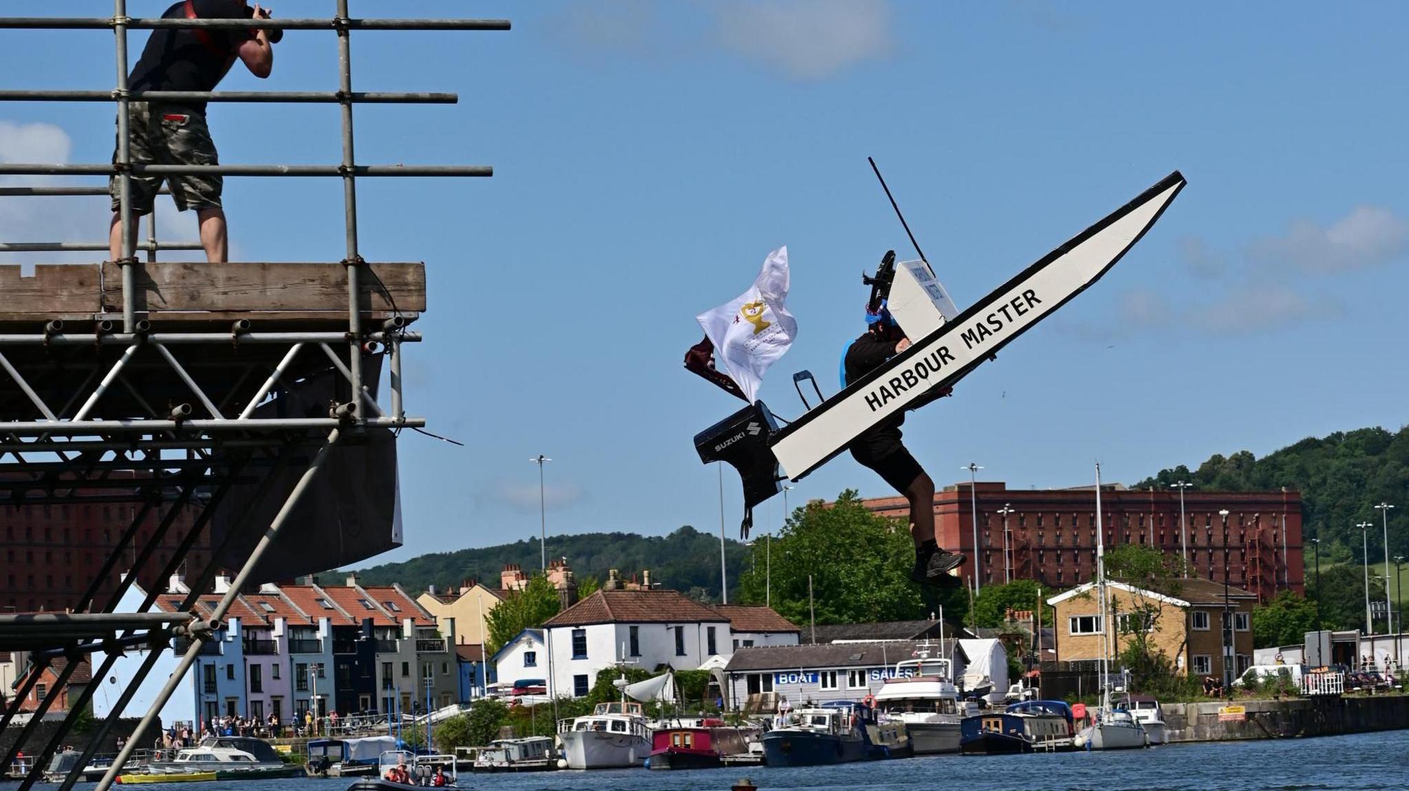 A competitor in the Bristol Birdman event takes off from the temporary scaffolding into the harbour. He is inside a design that is meant to look like the Harbour Master's boat