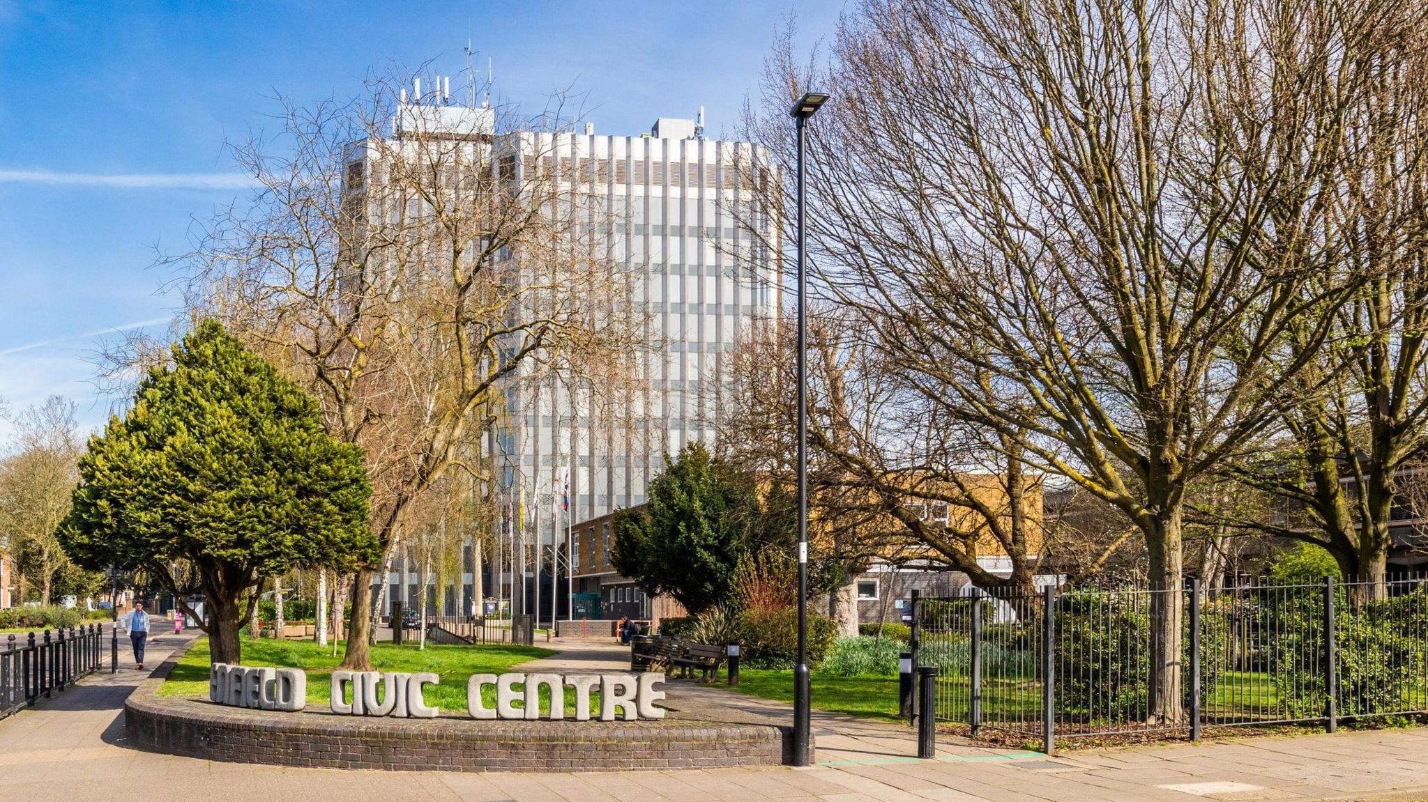 A general view of Enfield Civic Centre. There is a tree-lined pavement, and a street lamp. 