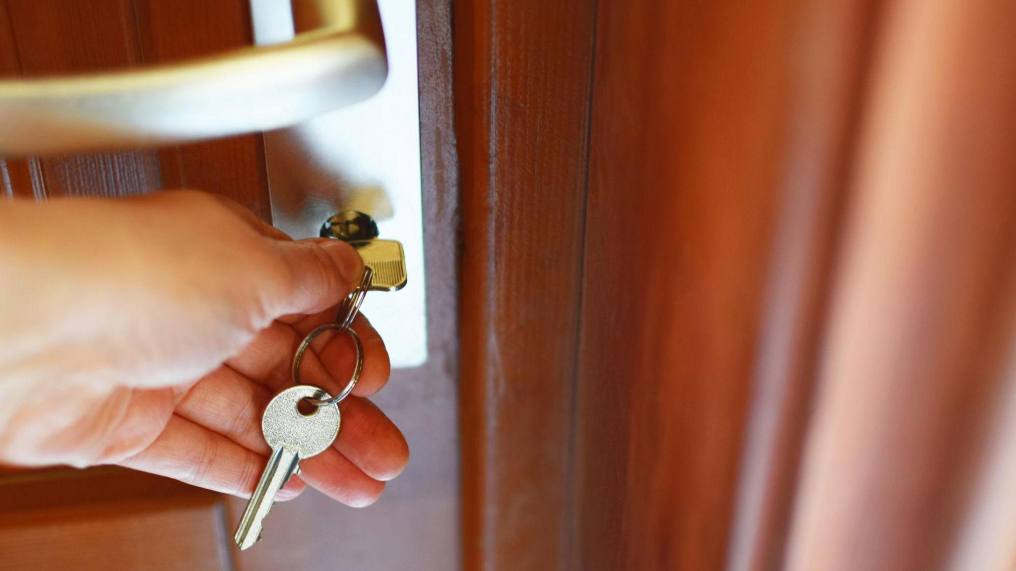 A close up image of a person putting a silver key into a wooden door lock.