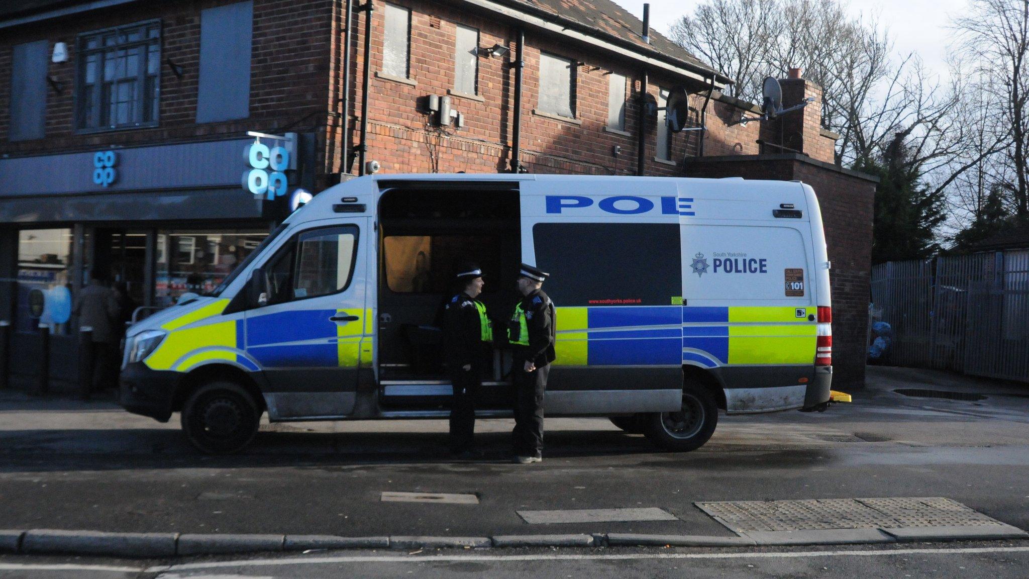 Two police officers chatting by police van parked in front of shops