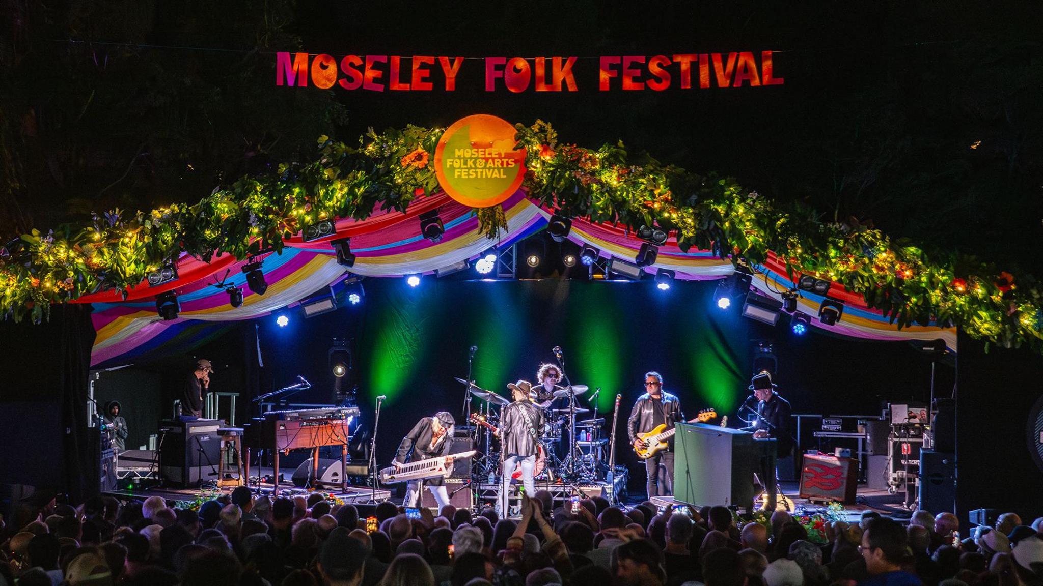 Moseley Folk Festival stage with Friday night headliners The Waterboys on stage which is lit in the darkness
