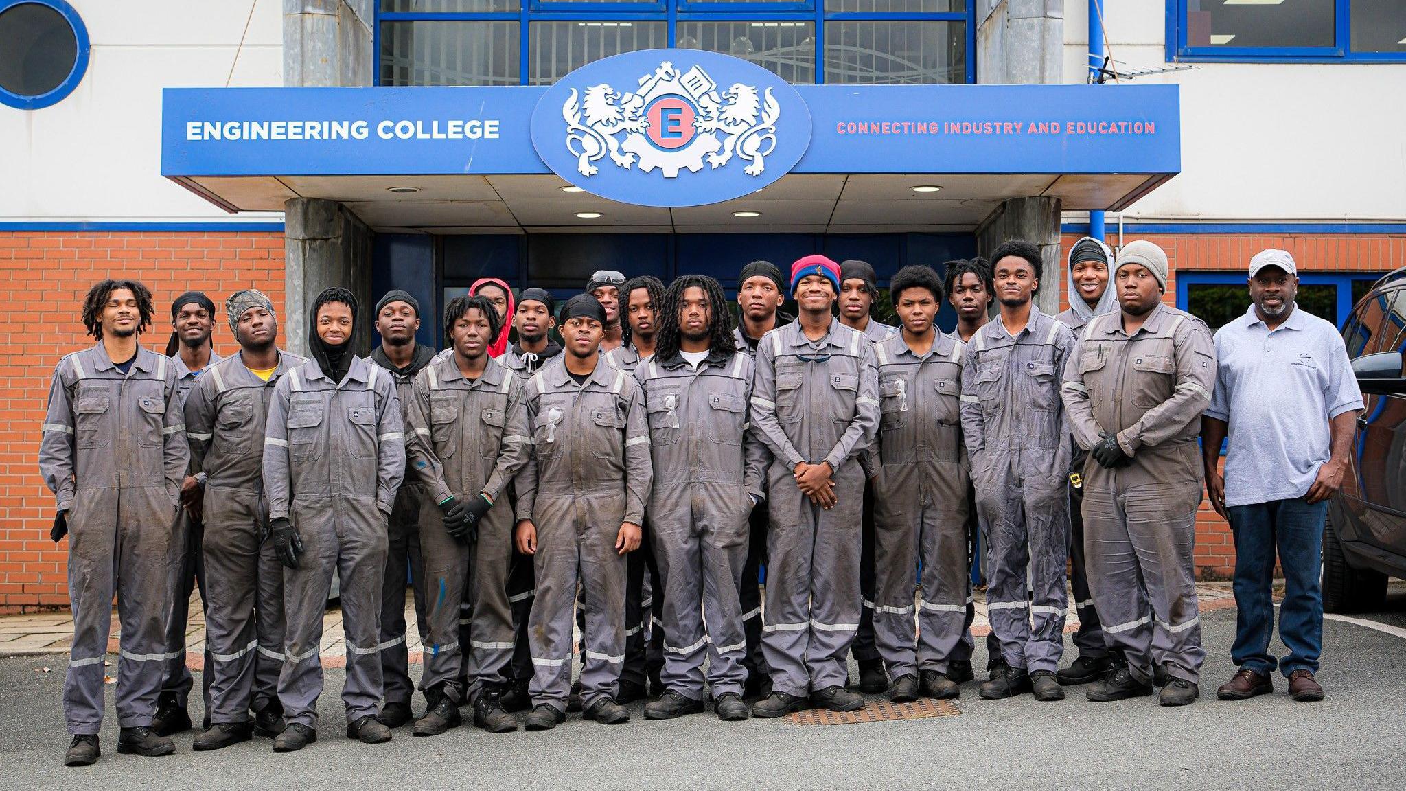 Twenty men lined up in grey overalls in front on the Engineering College entrance.
