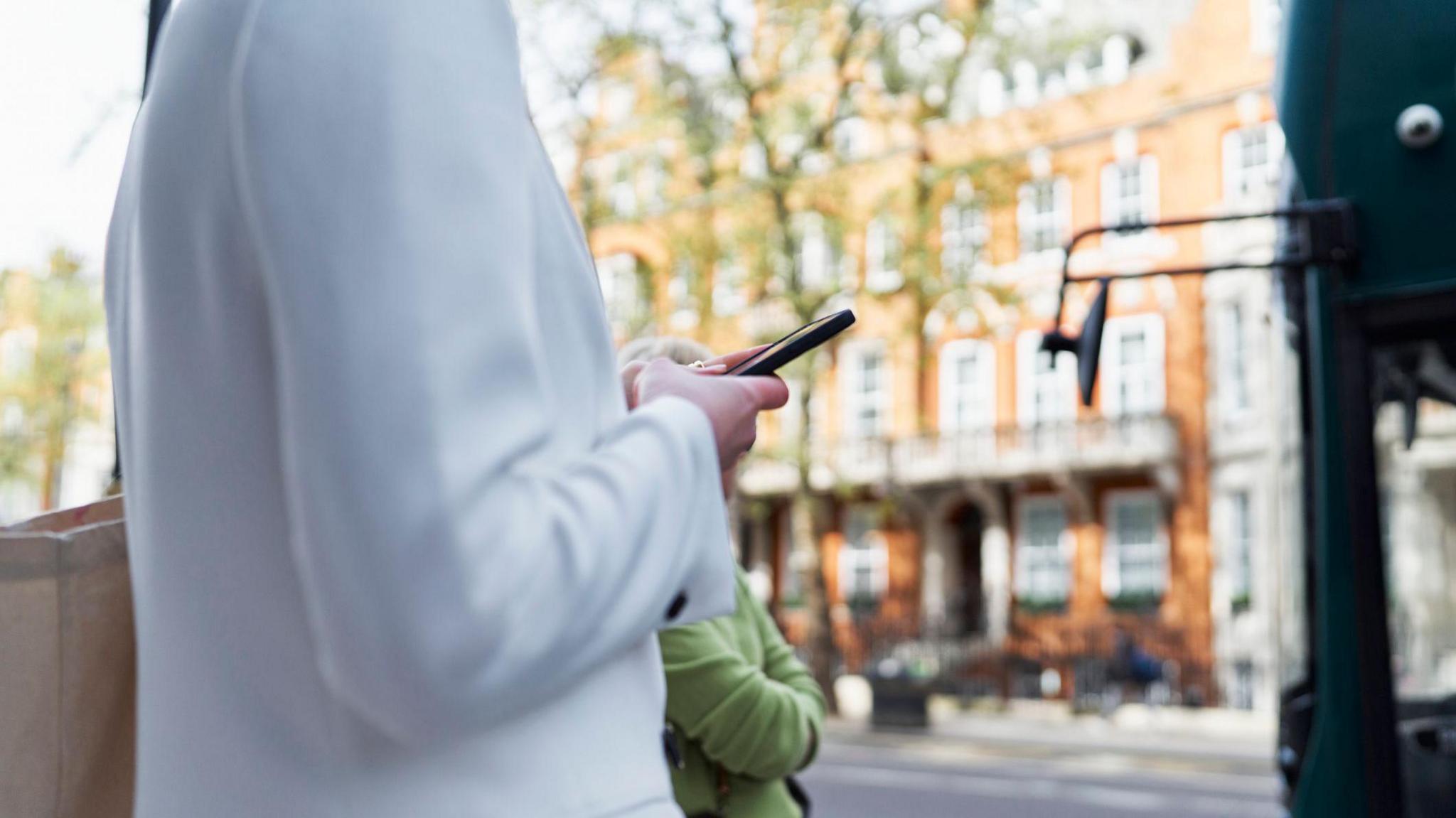 Woman in white cardigan looks at mobile phone in a London street