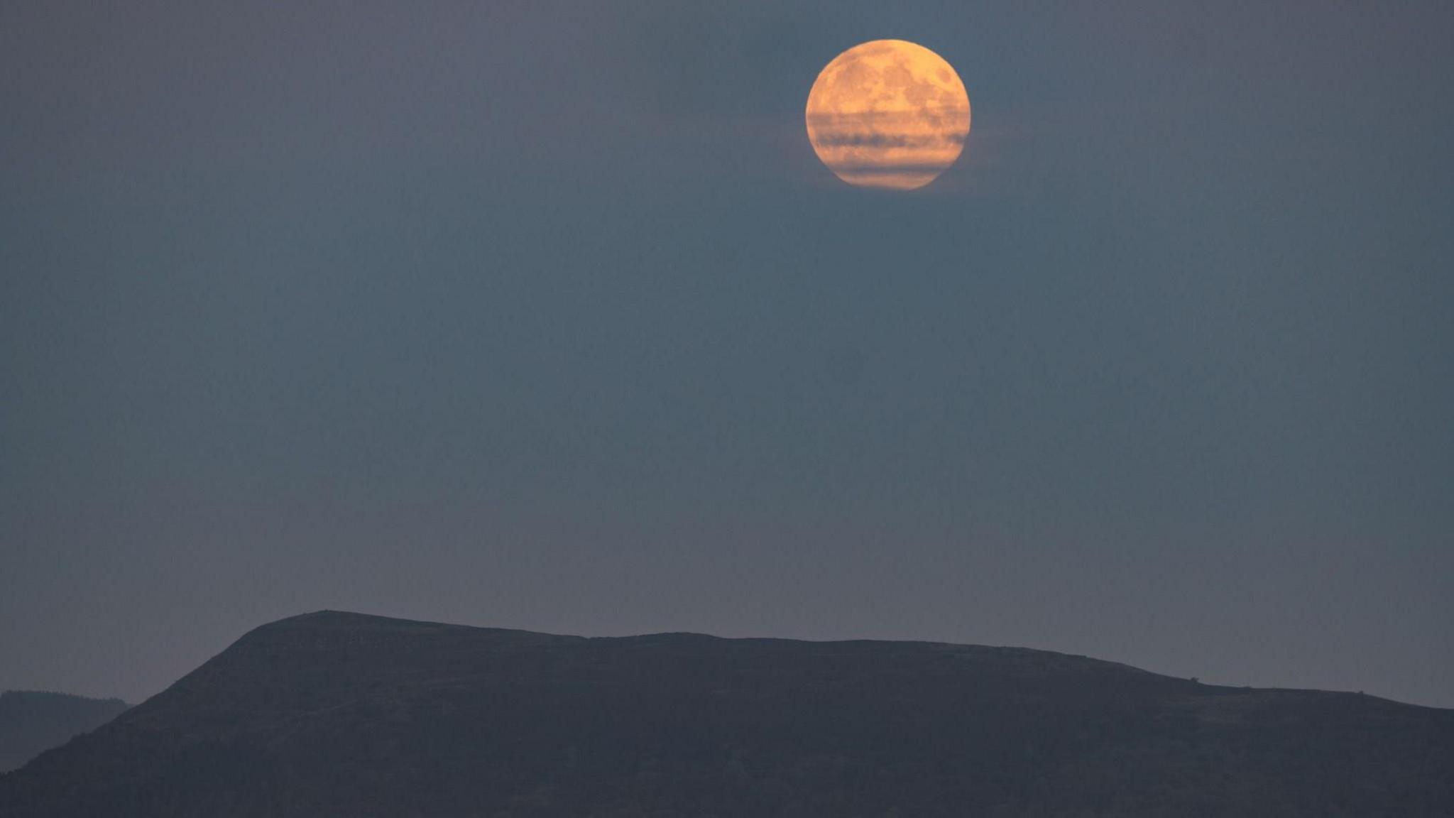 The supermoon is huge in the sky over Skirrid mountains. Clouds partially cover the moon.