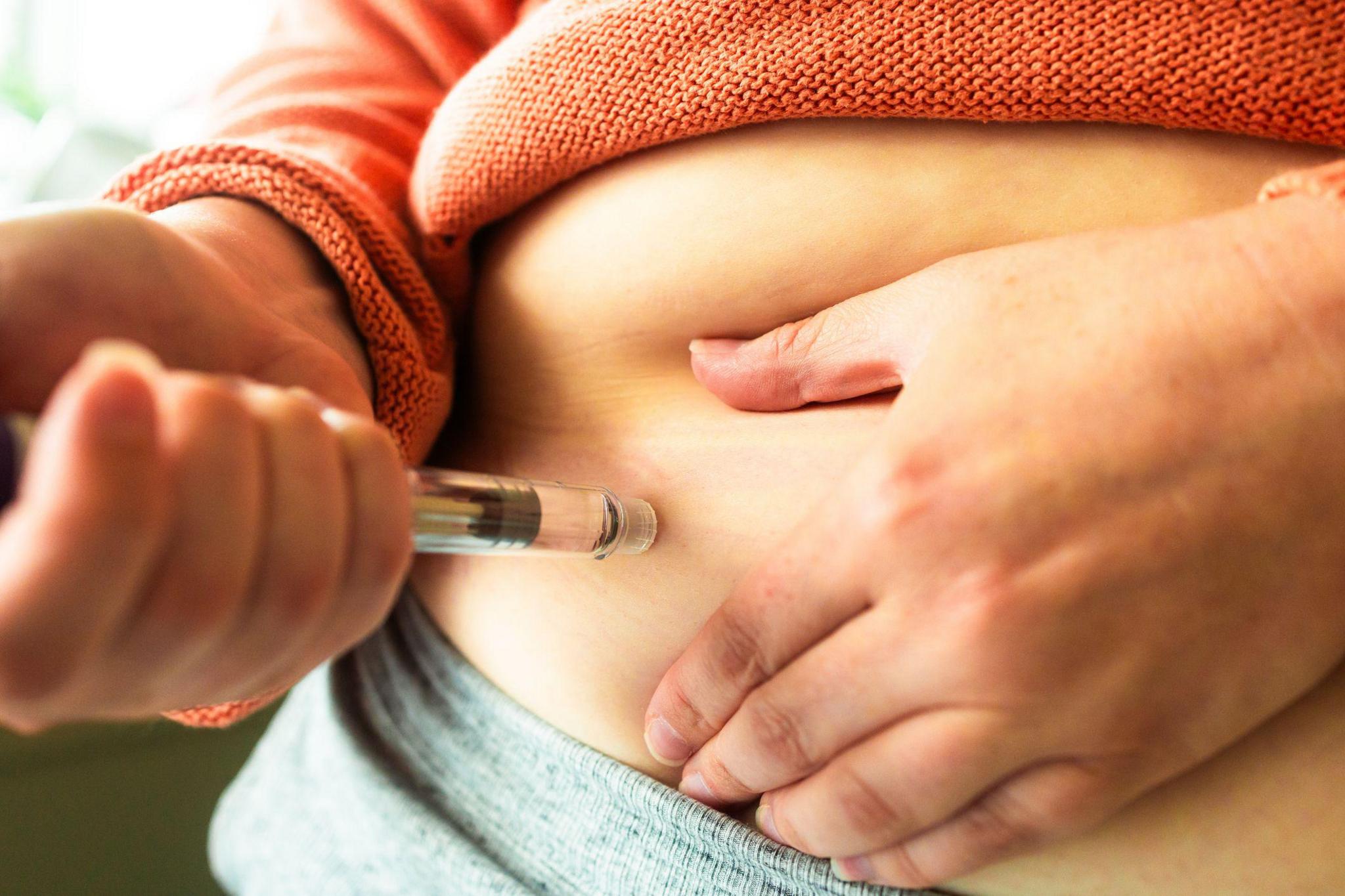 Close up of a woman's hands holding a weight loss injection pen. She is injecting the dose into her abdomen.