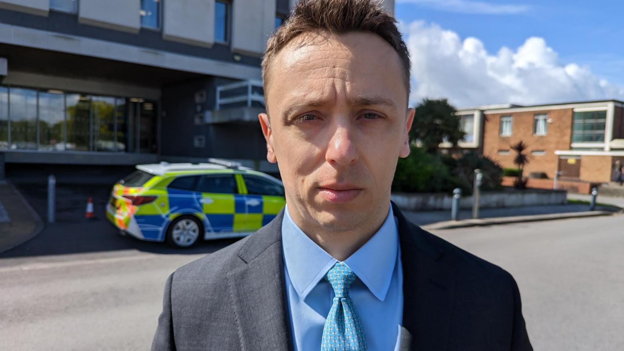 DCI Mark Almond standing outside court wearing a blue shirt and tie and grey jacket