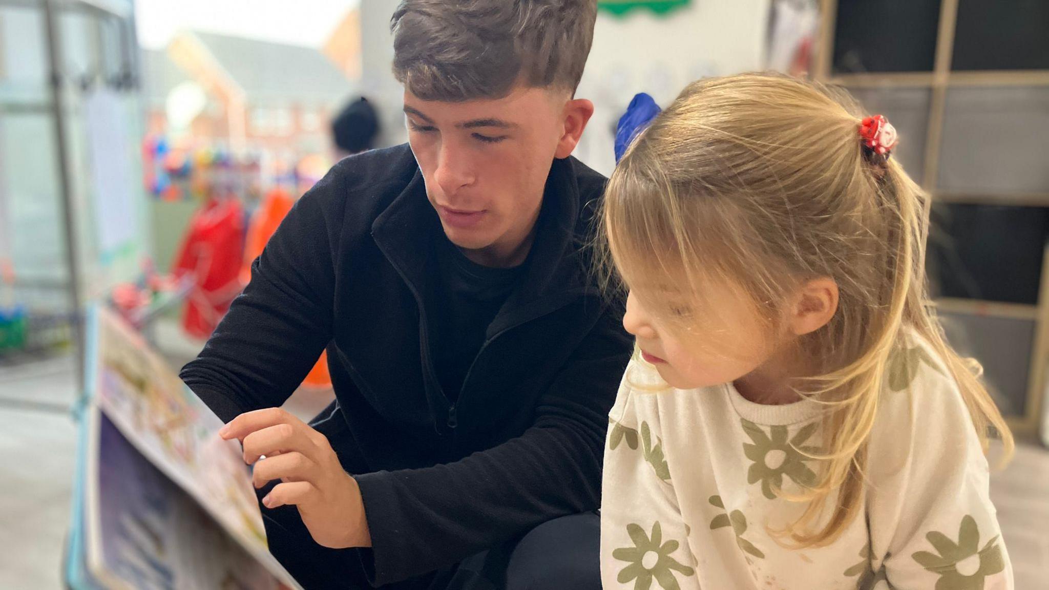 An early years staff member reads to a child inside a nursery classroom